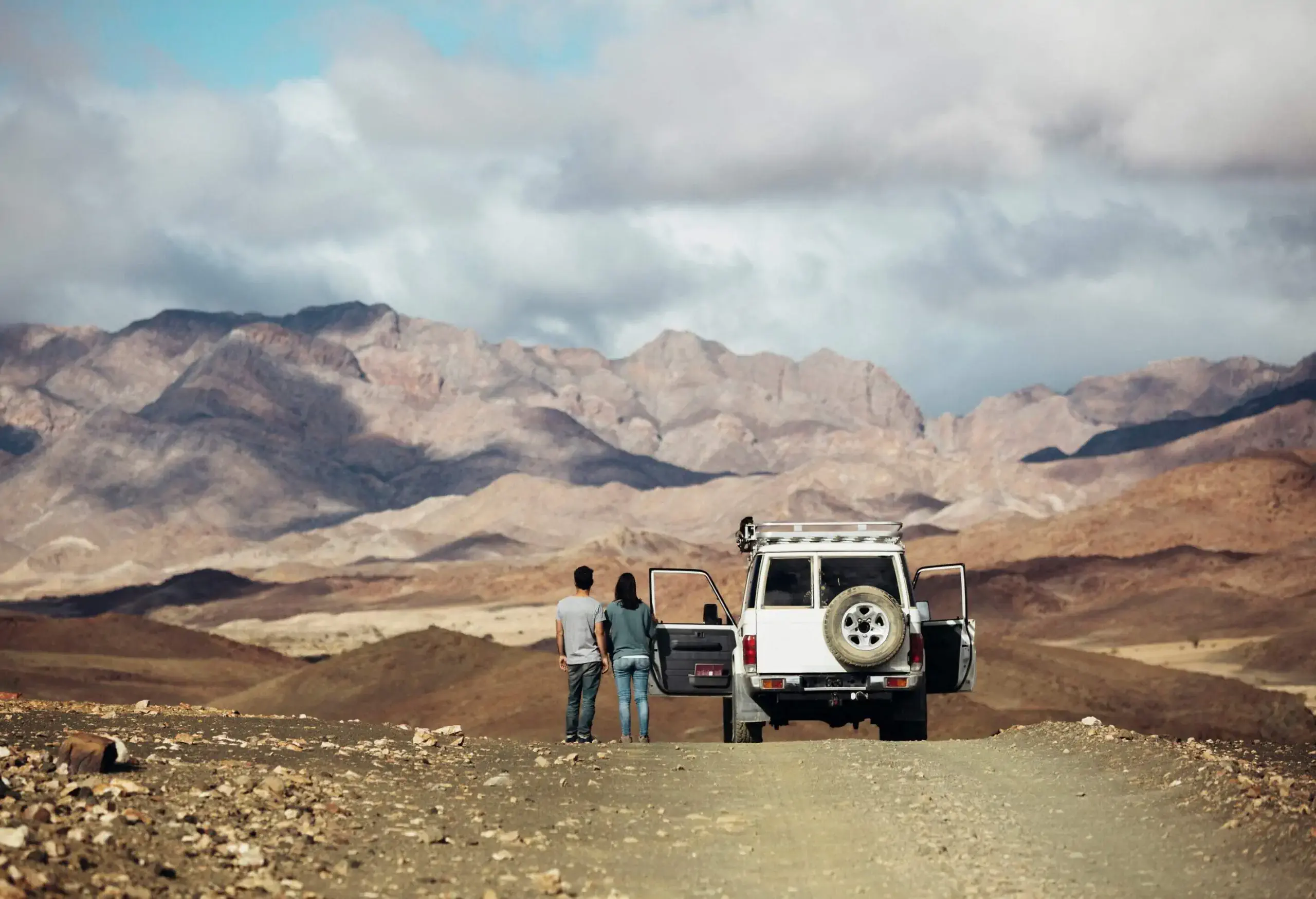 A couple standing next to a car in the desert