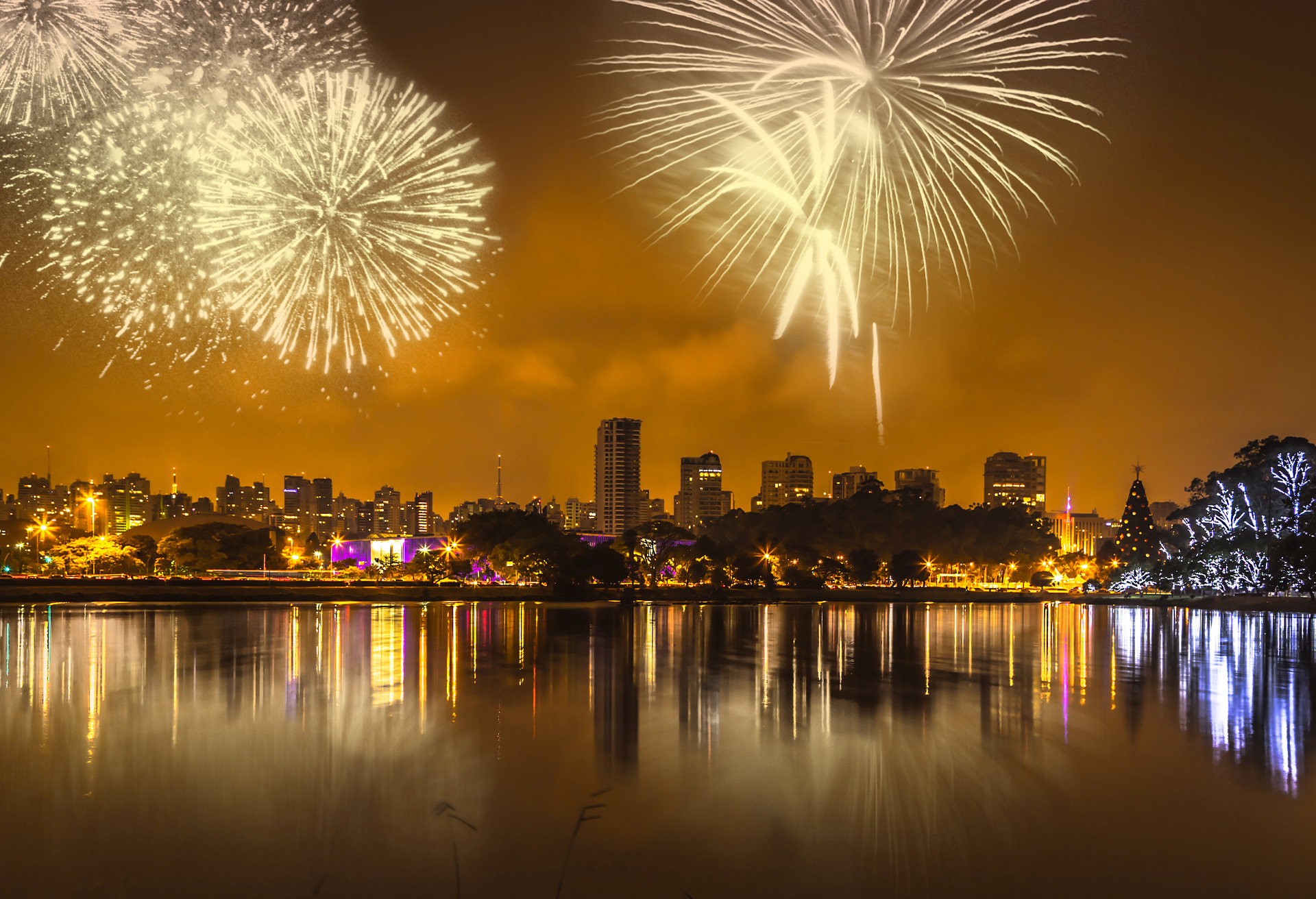 foto de uma cidade à noite, na beira de um rio, iluminada por fogos de artifício