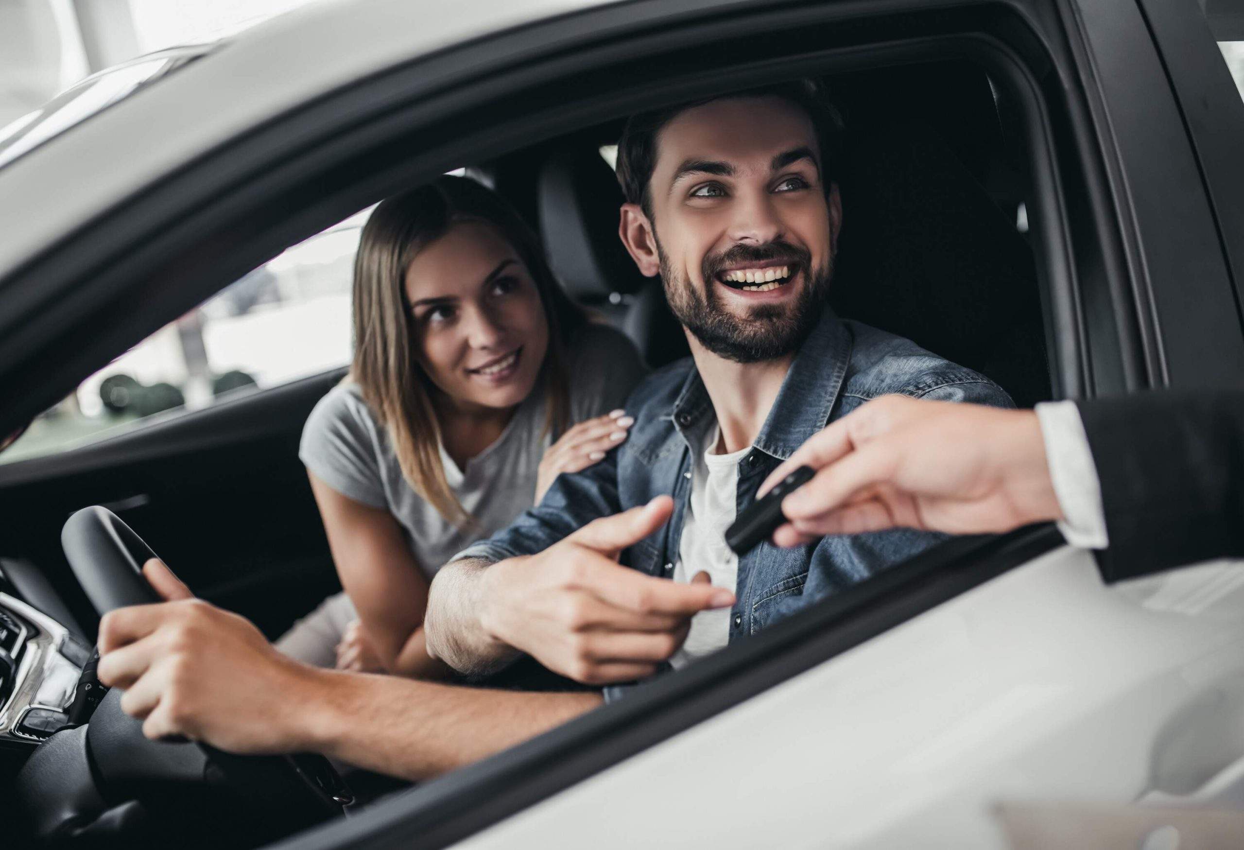 Two happy individuals inside a car look out the driver's window.