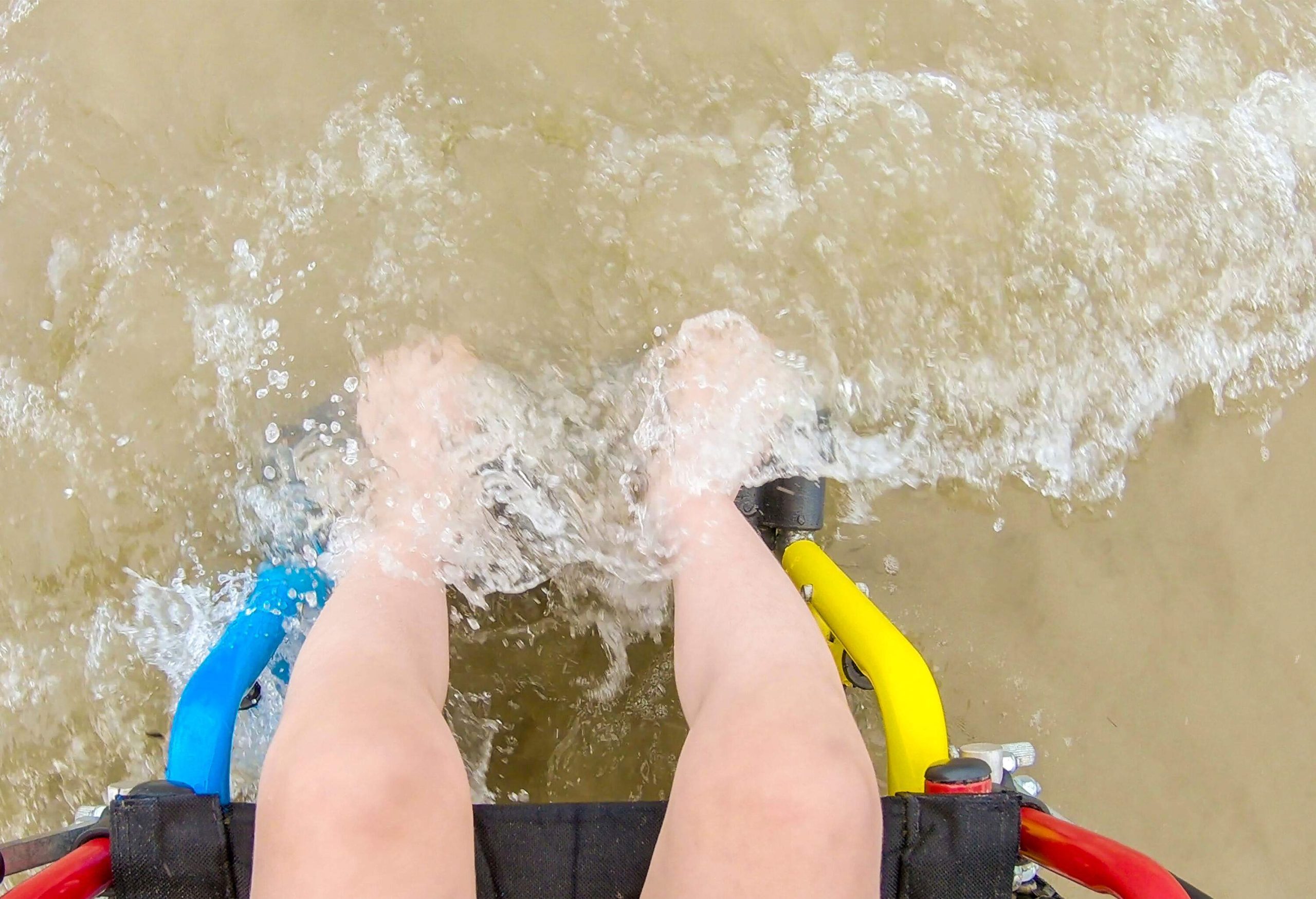 A wheelchair-bound person's feet being swashed by the waves.