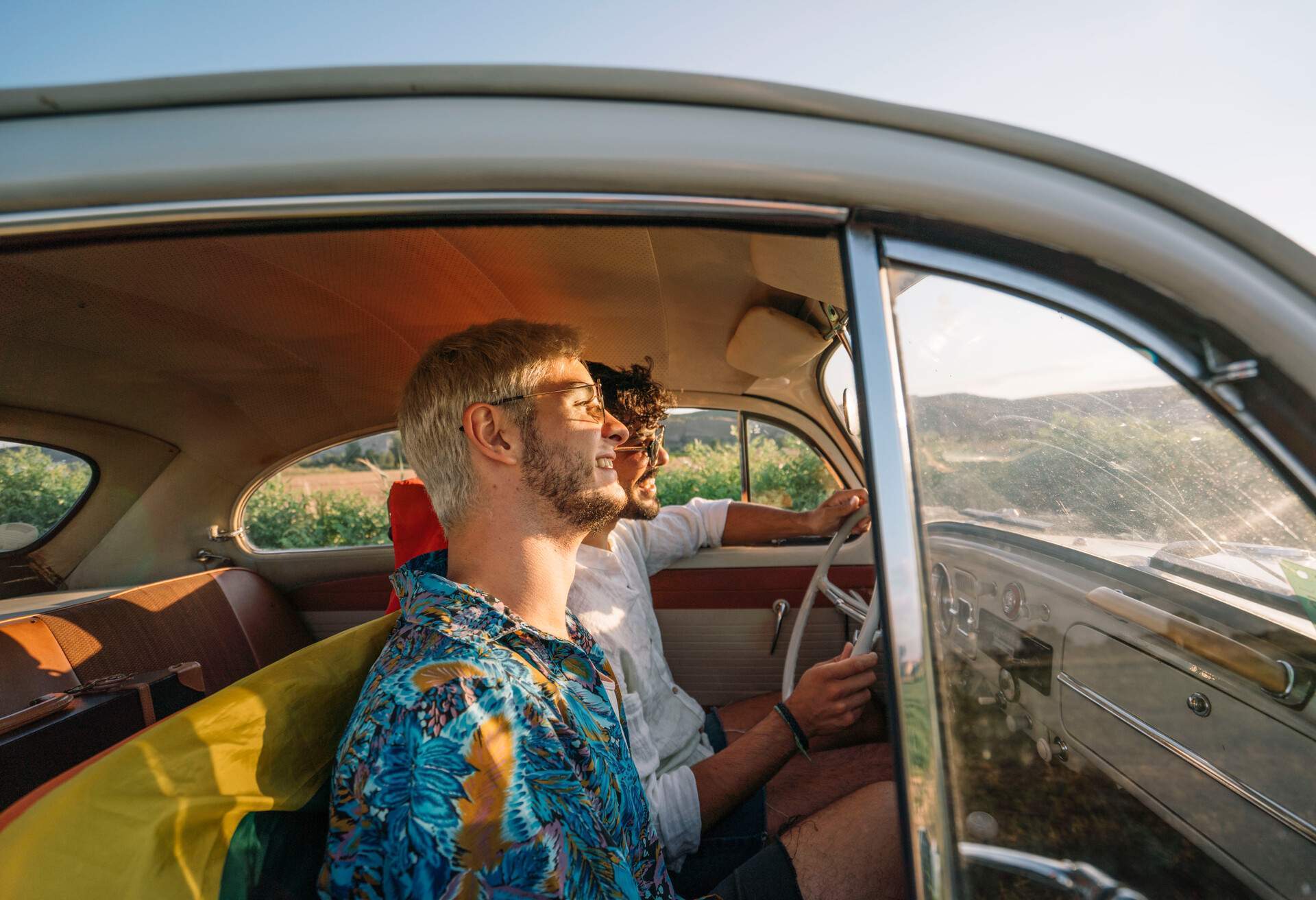 Two young men in an old car, smiling with a nice sunset light