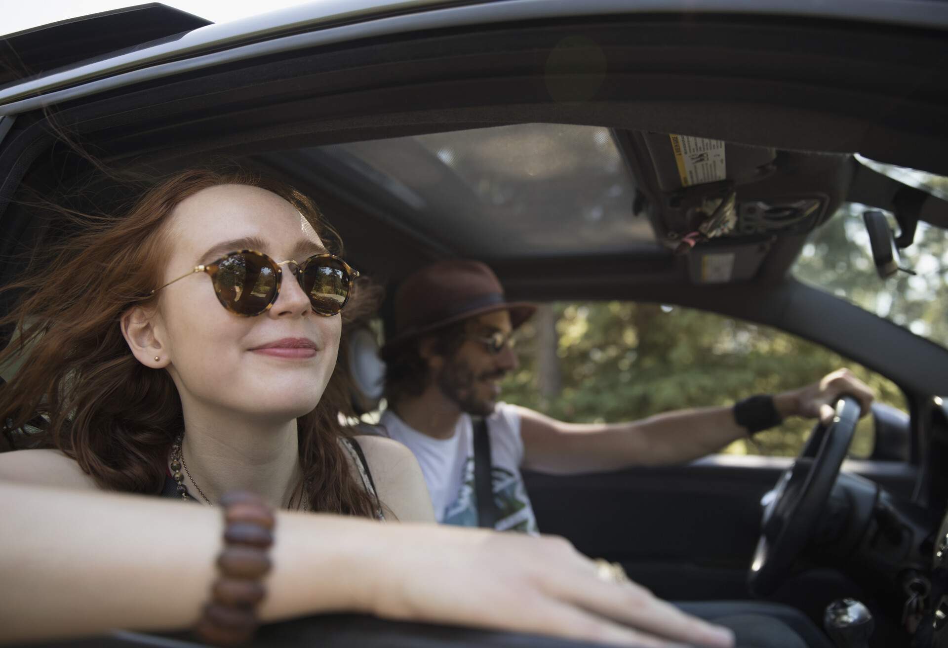 A smiling woman seating in a car, and a man driving the car