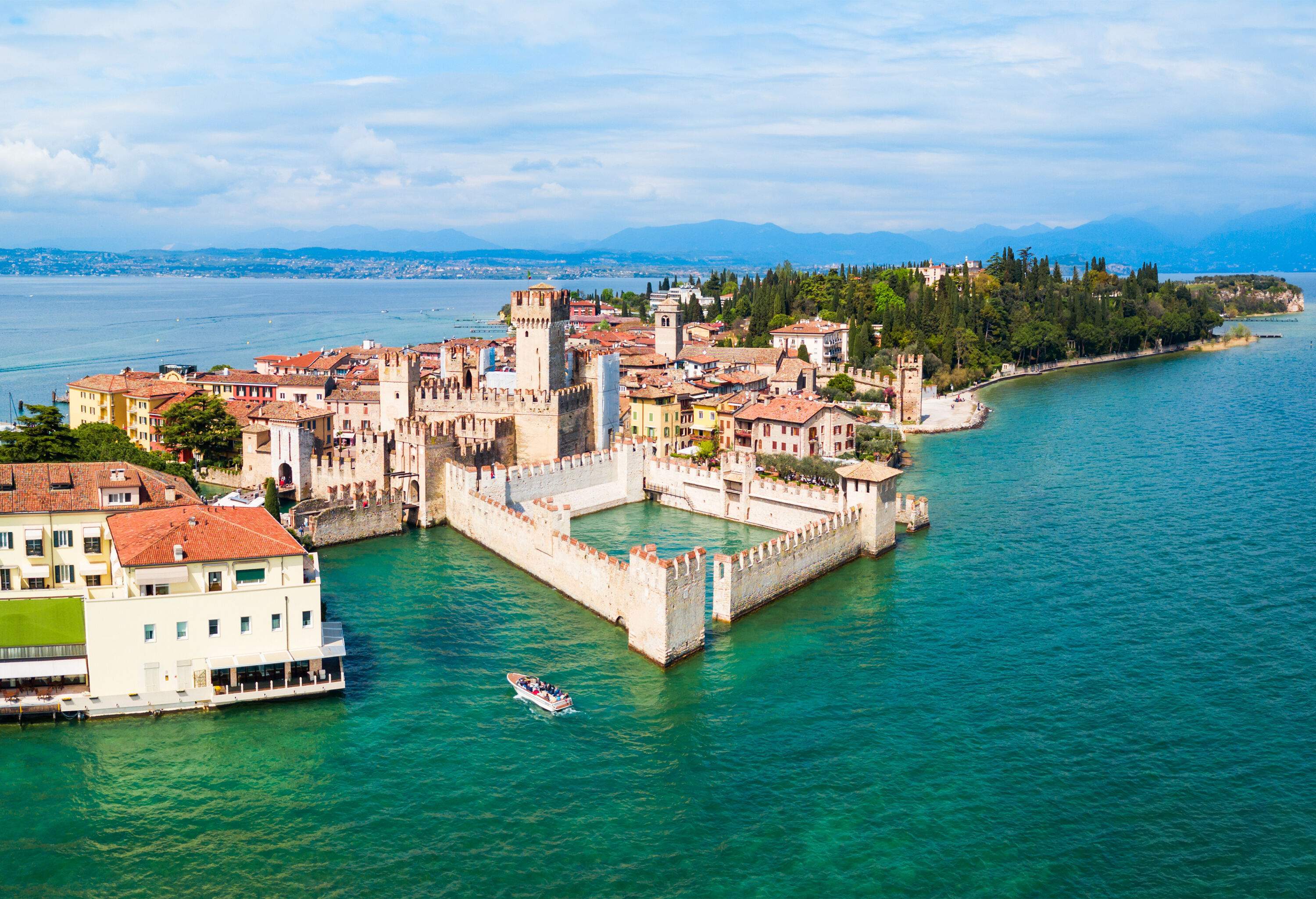 Panoramic view of a fortress stone castle on the shore of the turquoise water lake among the old buildings of a town on the edge of a lush island.