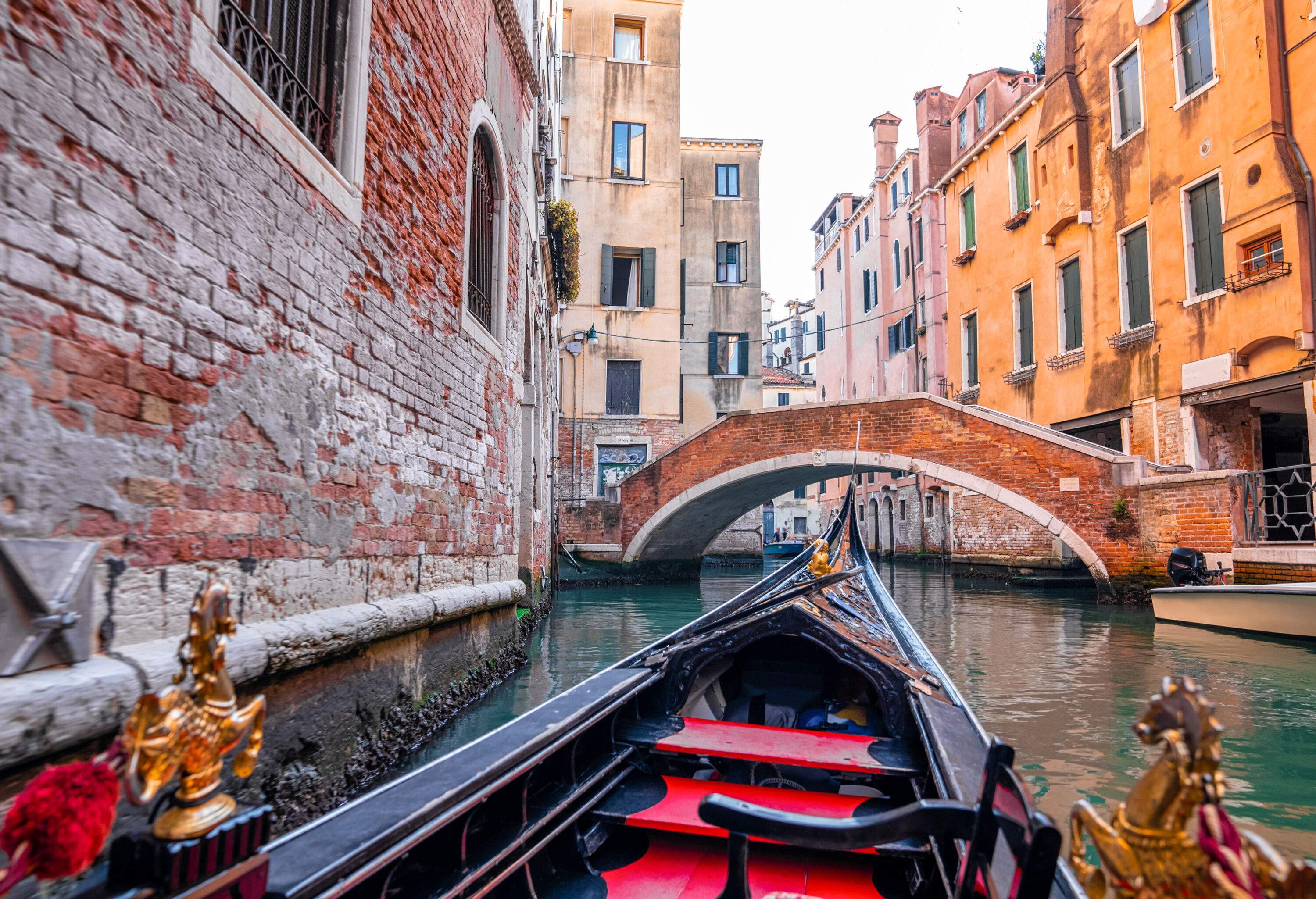 A gondola with views of an arch bridge across a water canal between tall buildings.