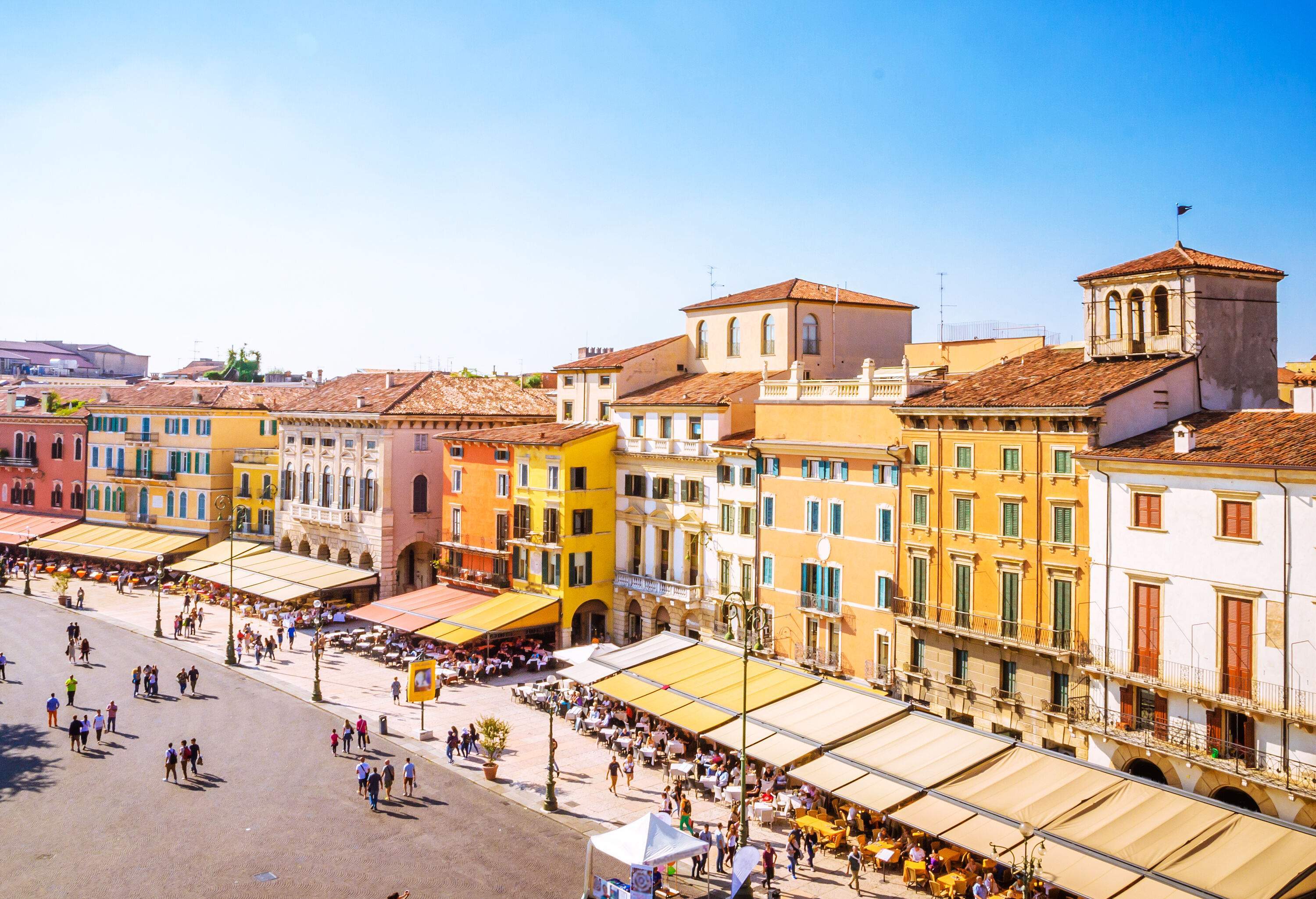 A lively central square is surrounded by a brilliant mix of colourful buildings that hold businesses and cafes, with people strolling around slowly.