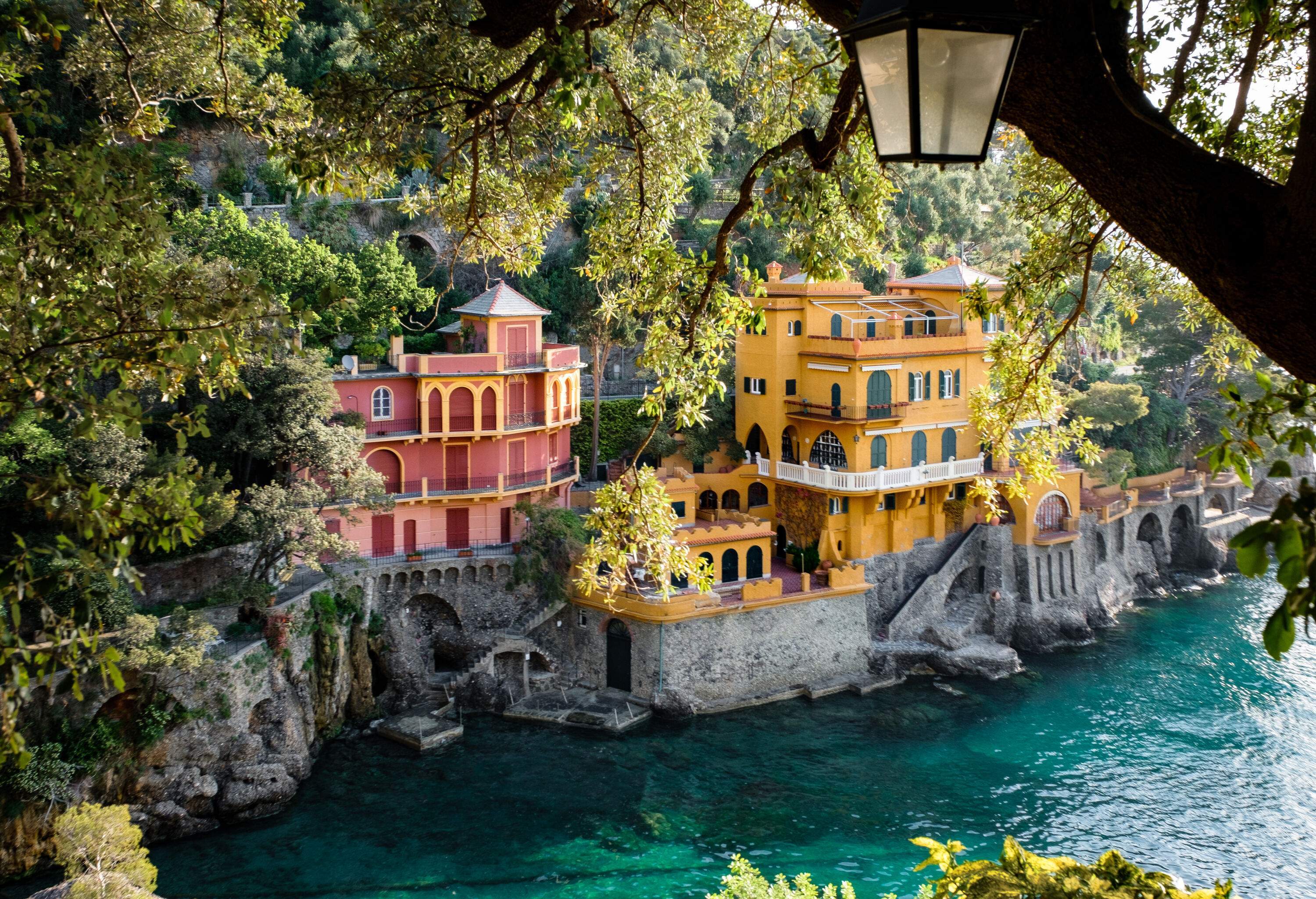 A yellow and red villa at the edge of a cliffside coast framed by tree branches.