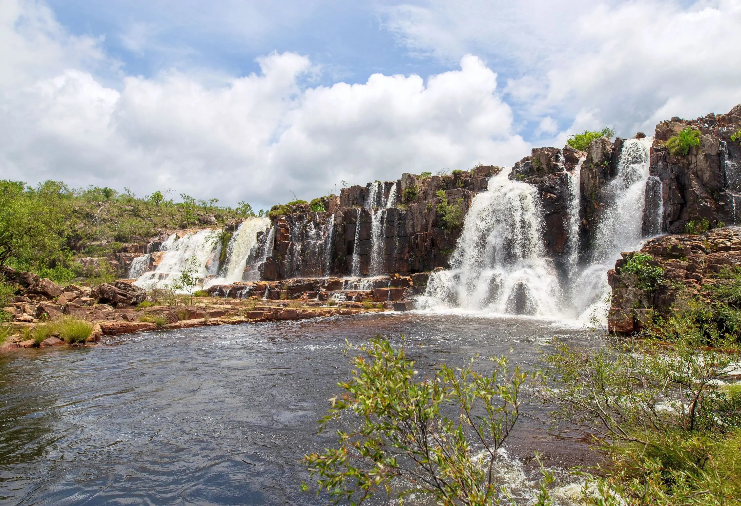 A steep cliff with cascading waterfalls that pours into a river.