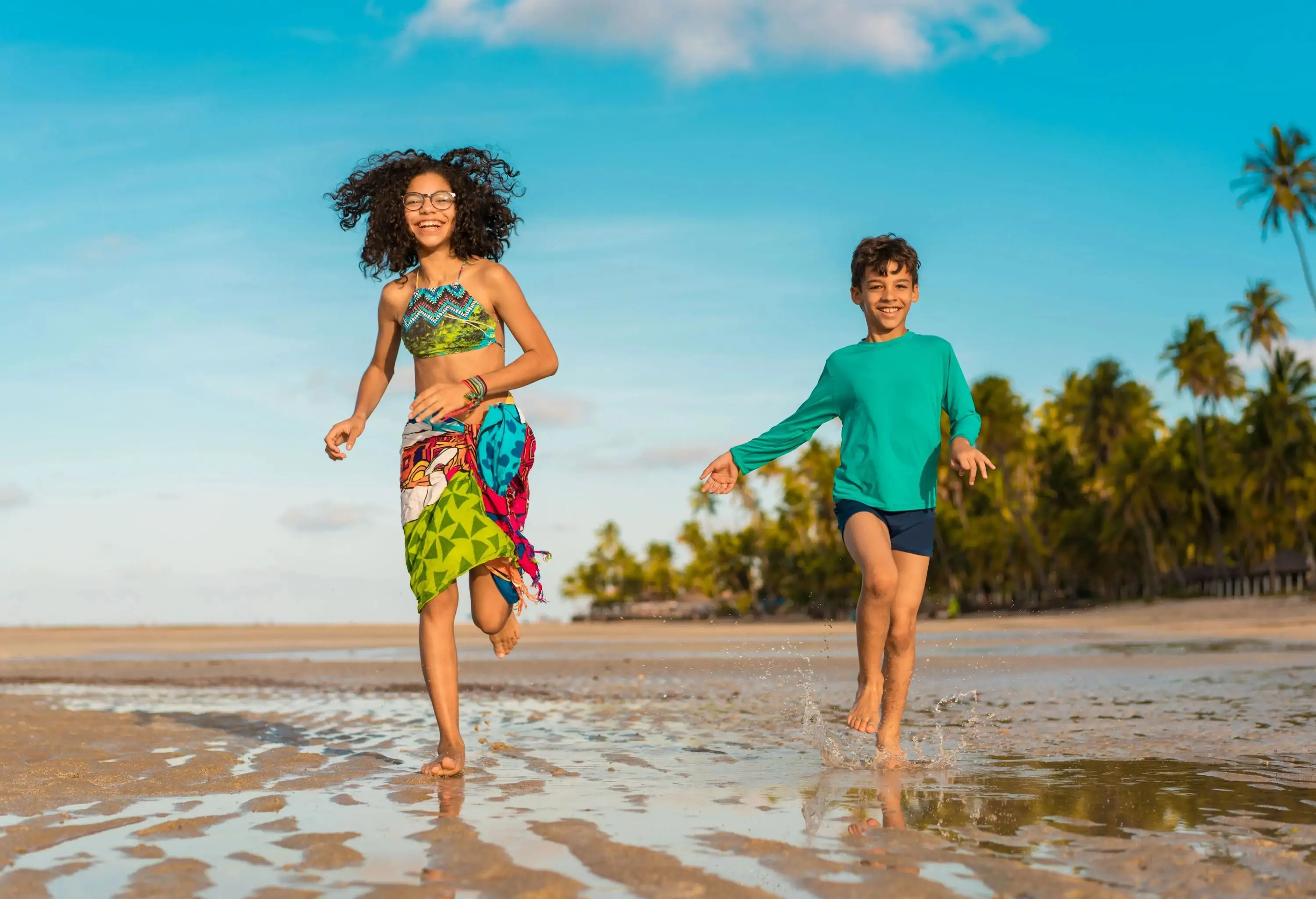 A happy sibling in their swimwear runs on the shore.