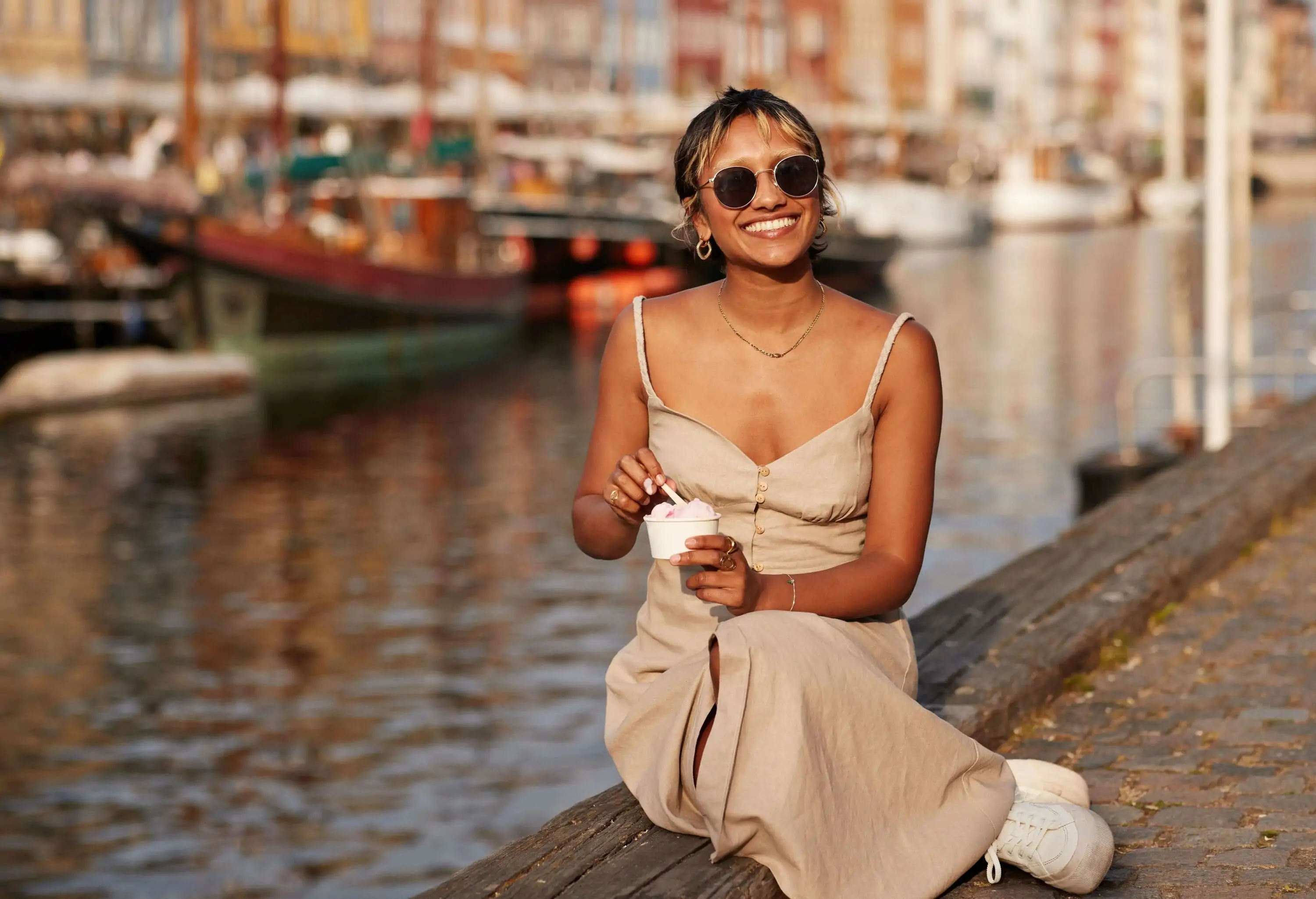 Happy young woman with ice cream cup wearing sunglasses while sitting on promenade
