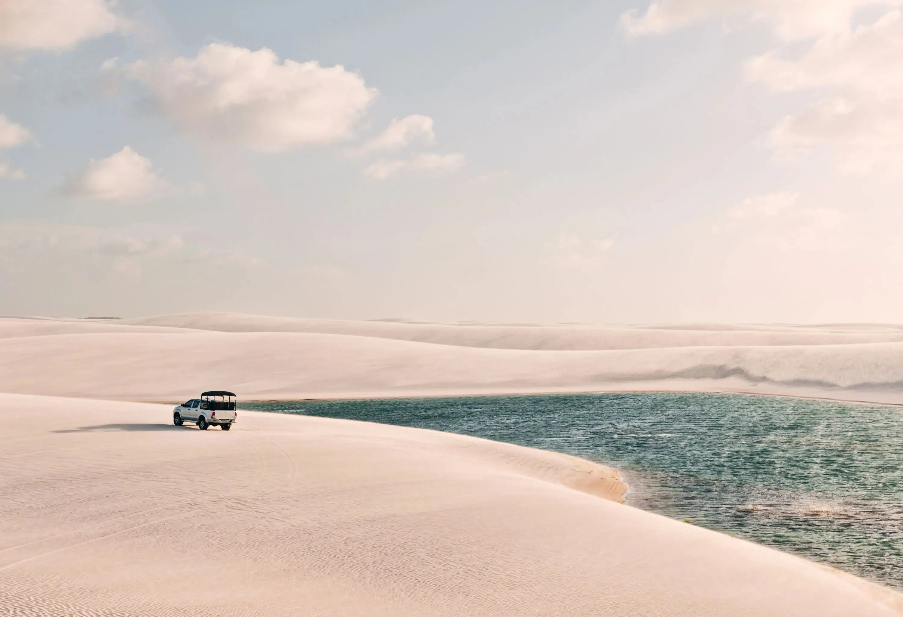 A car parked on the expansive white sand dunes by the river.