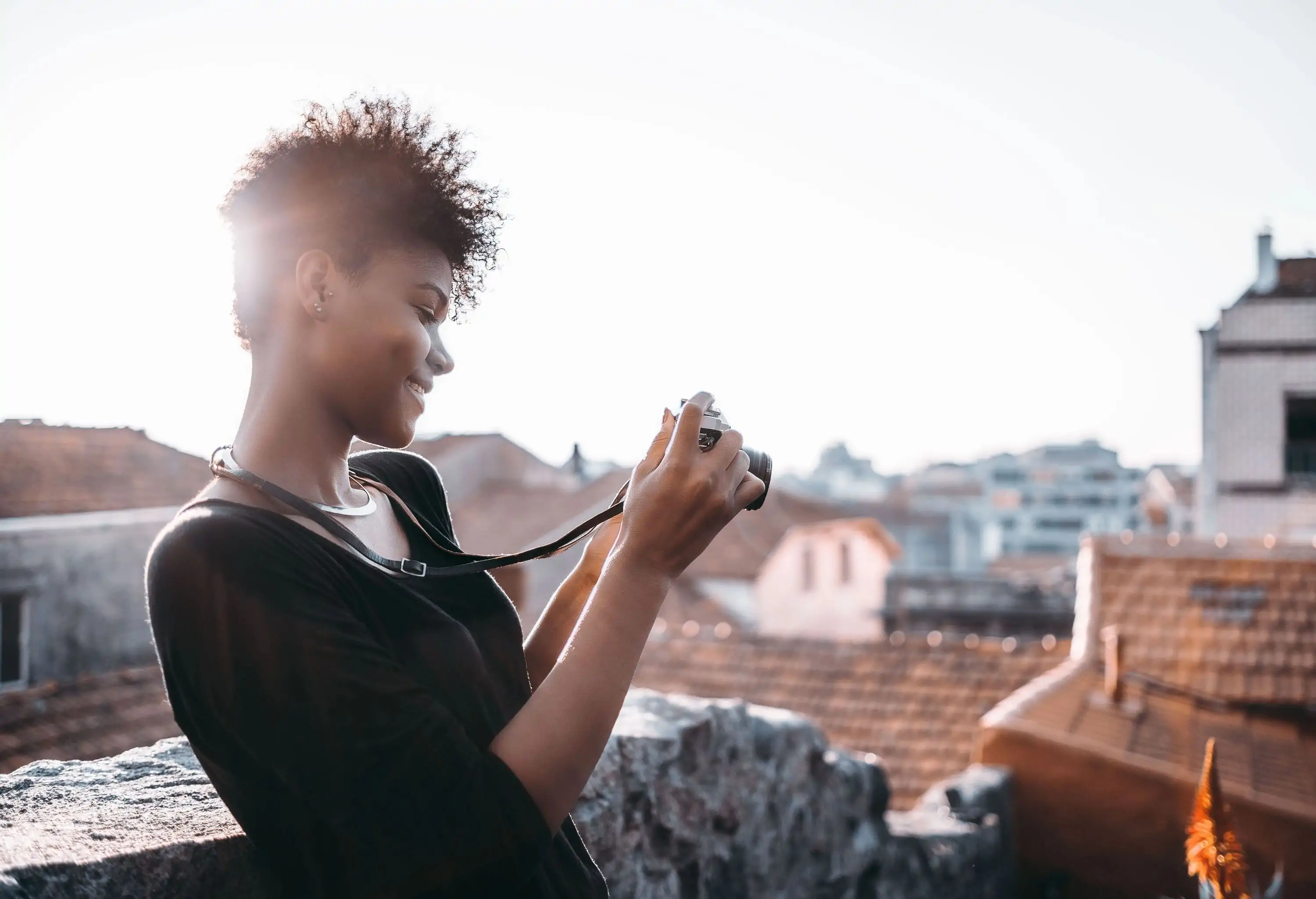 A curly-haired woman smiles as she scans through her digital camera's images.