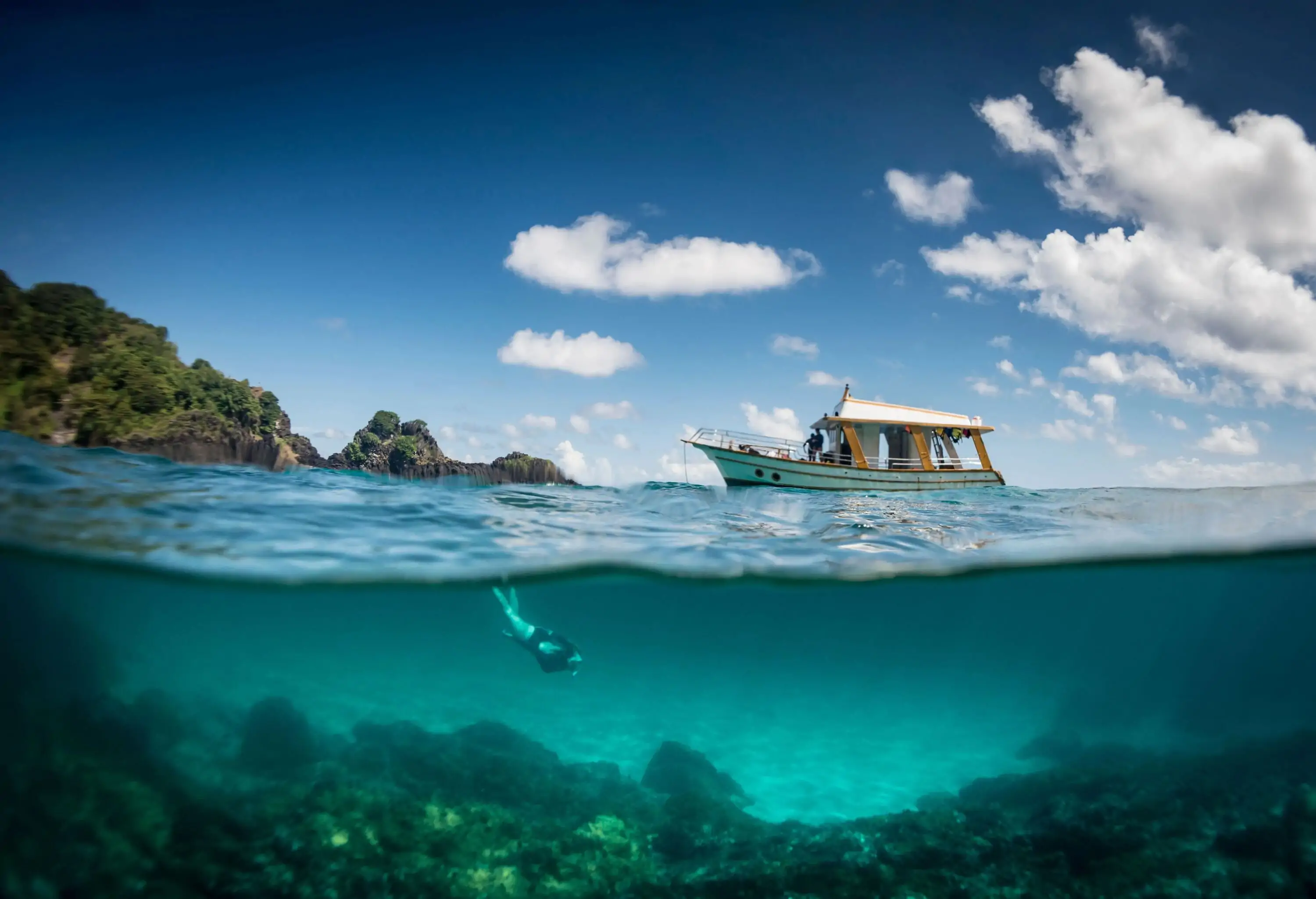 A diver delving to the bottom of the sea with a boat bobbing on the surface.