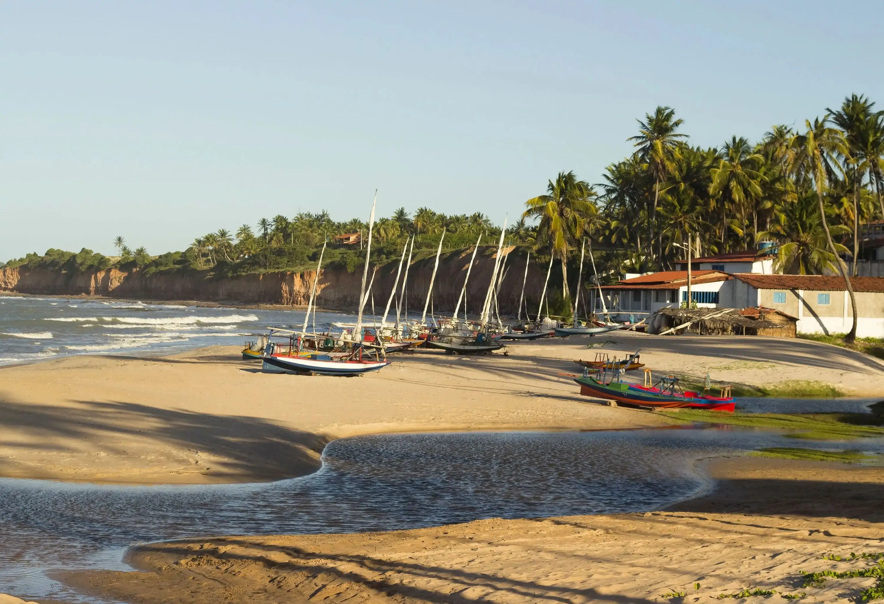 Wooden fishing boats parked on the beach, which is bordered by sandy cliffs and tropical vegetation.