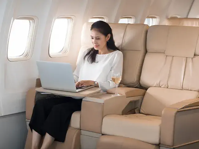 foto de uma mulher branca asiática trabalhando em um laptop em uma poltrona de business class de avião