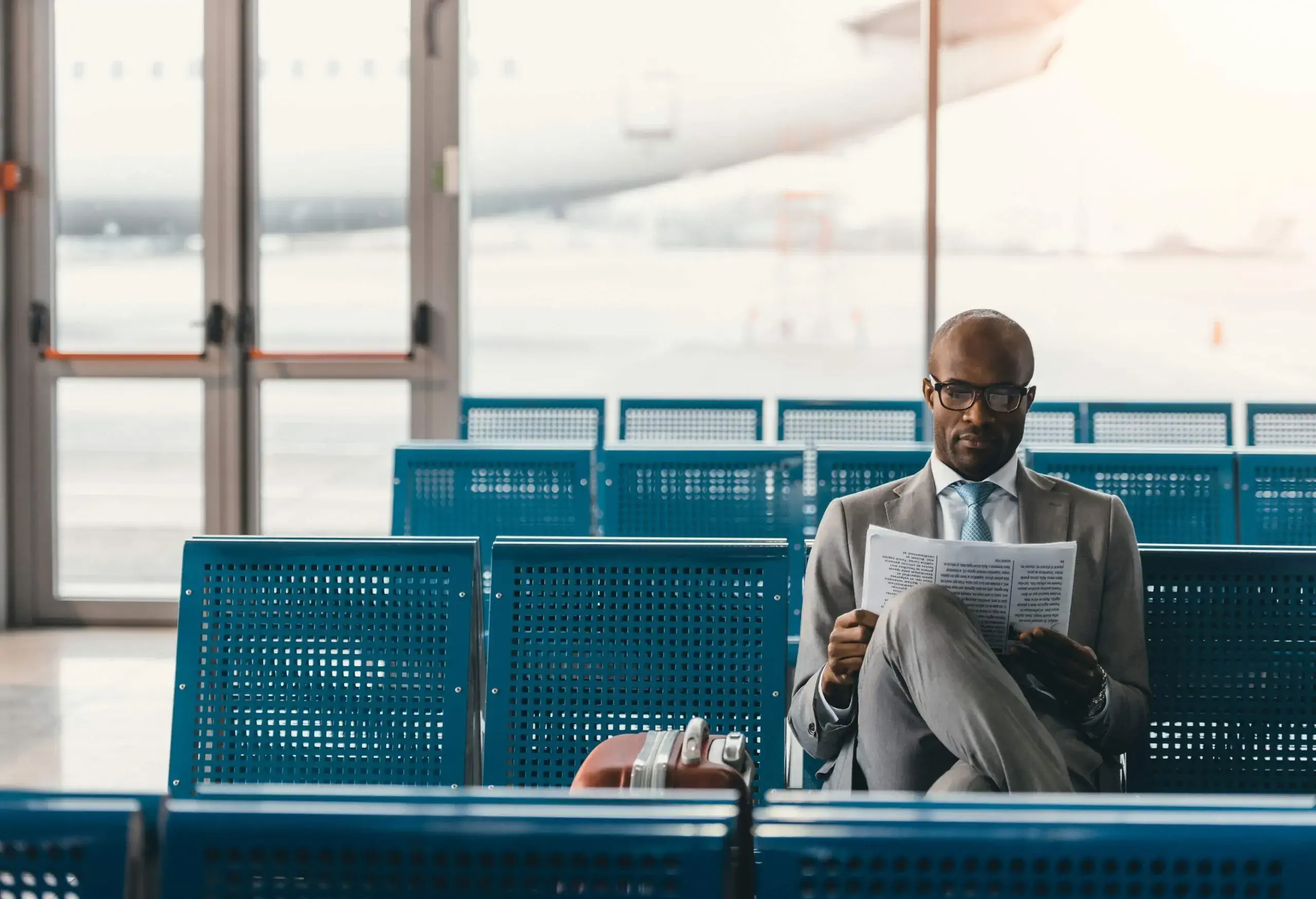 A businessman reading a paper while sitting in one of the terminal's row seats.