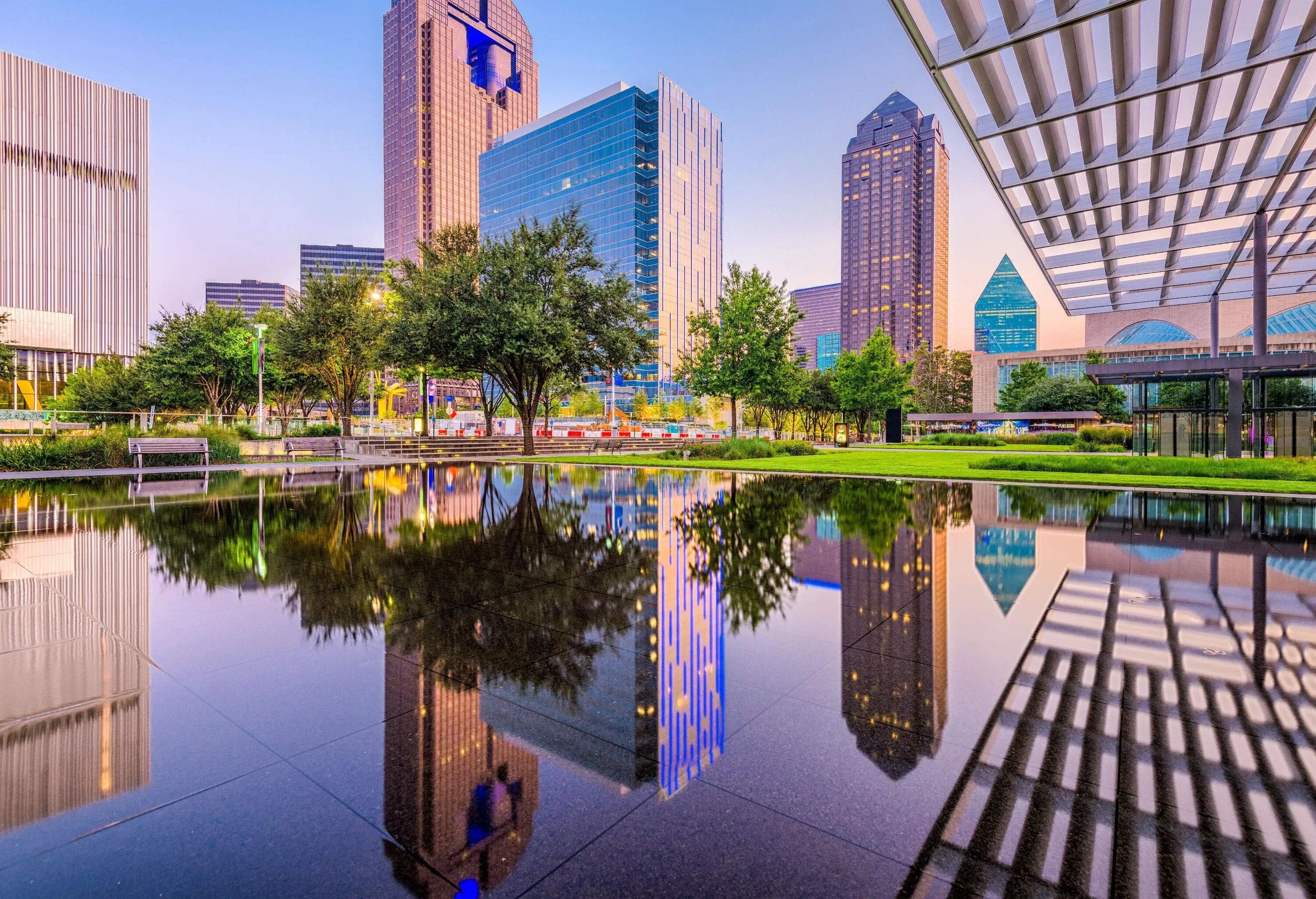 A pool of water in a forested park reflects the surrounding high-rise buildings in the city.