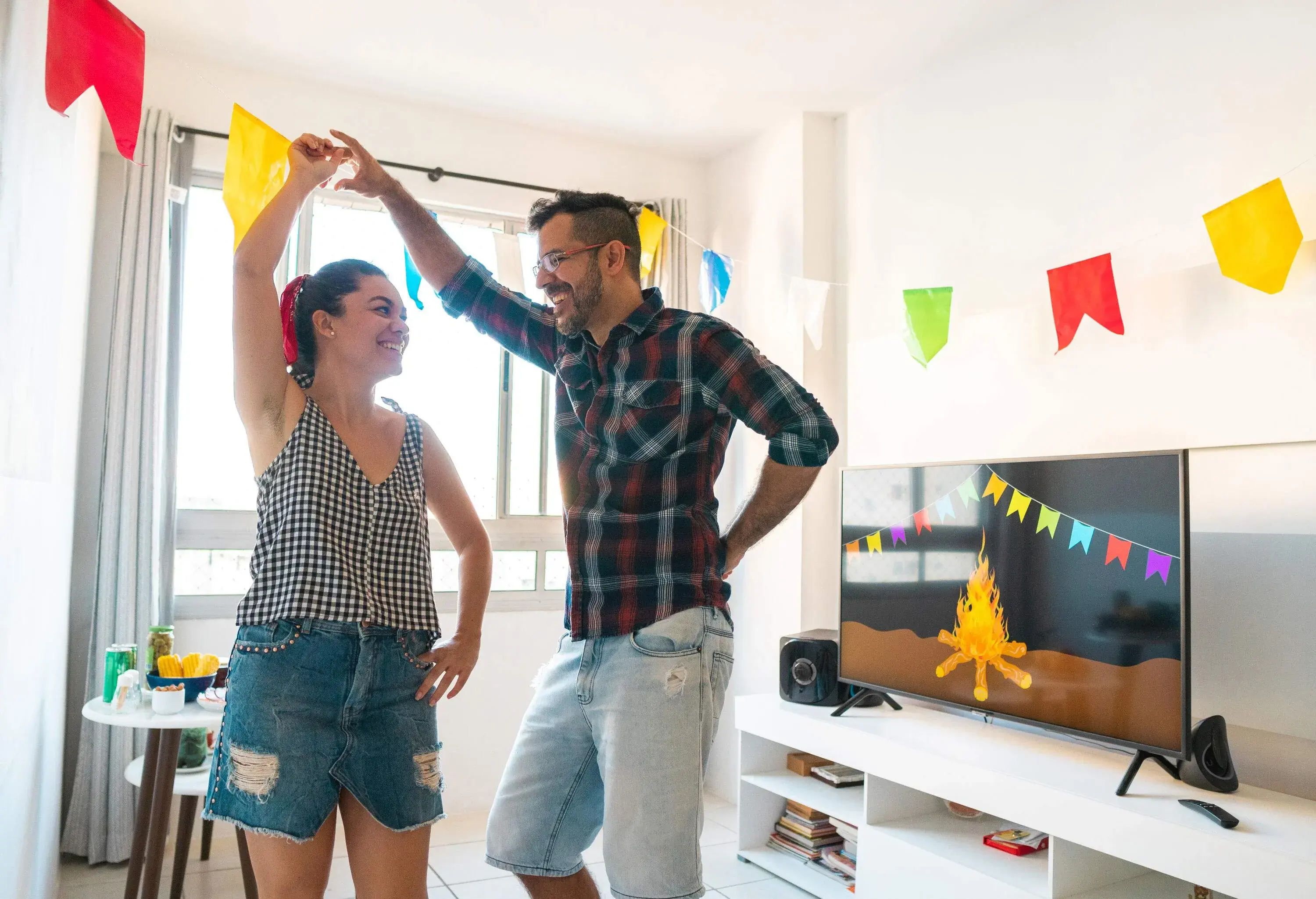 A loving couple hangs cheerful pennant banners in their living room, sharing a smile of accomplishment and affection as they create a festive atmosphere together.