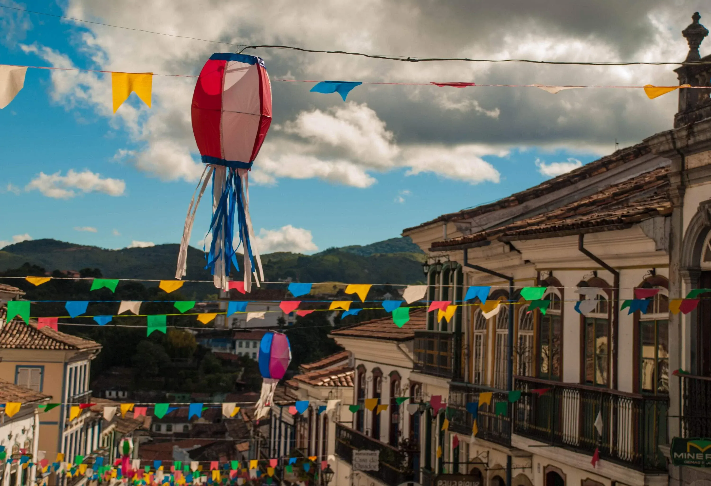 Uma rua em um bairro residencial com faixas coloridas de festivais penduradas e lanternas decoradas.