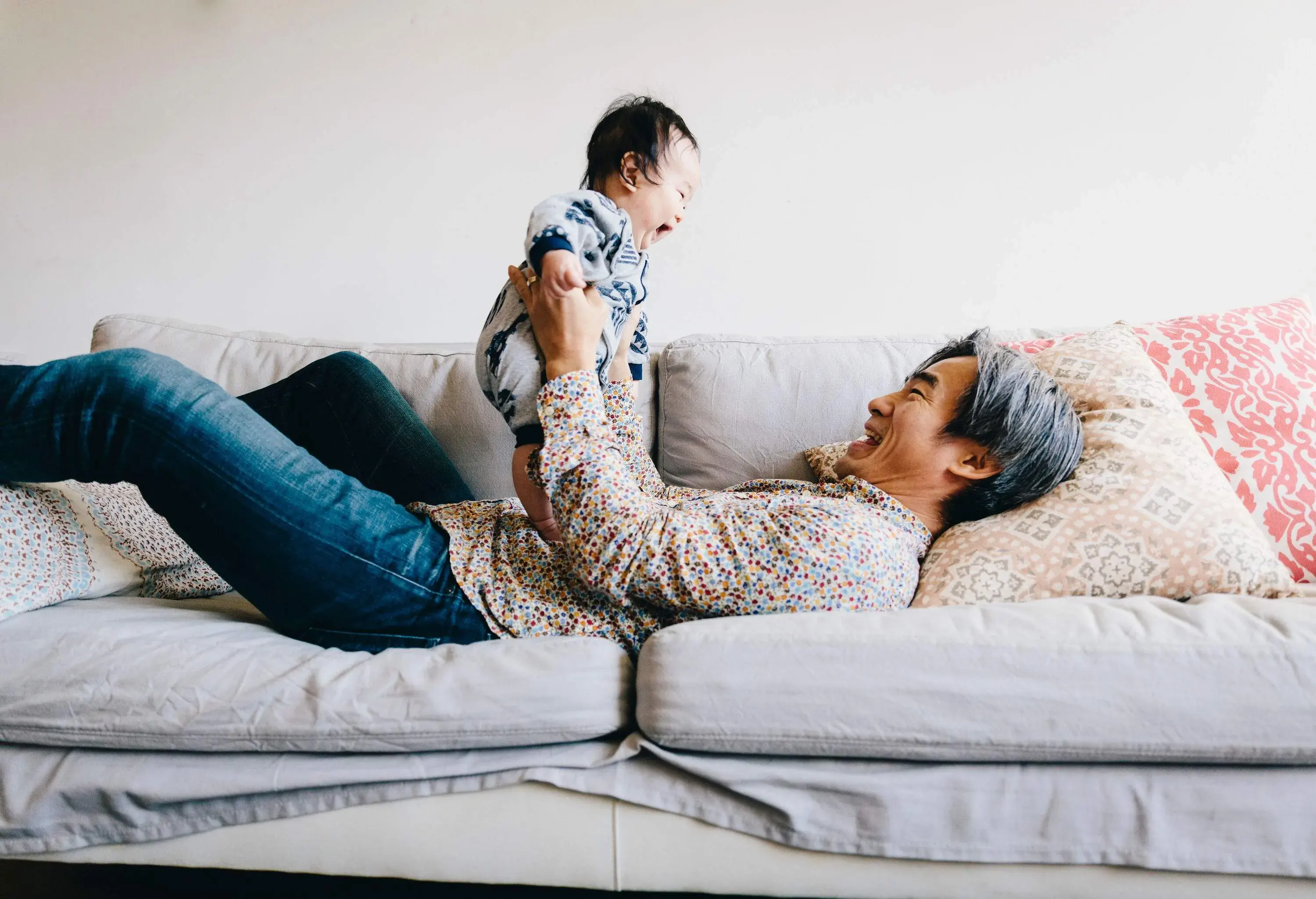 A grandfather lying on his back on a couch and playing with a baby.