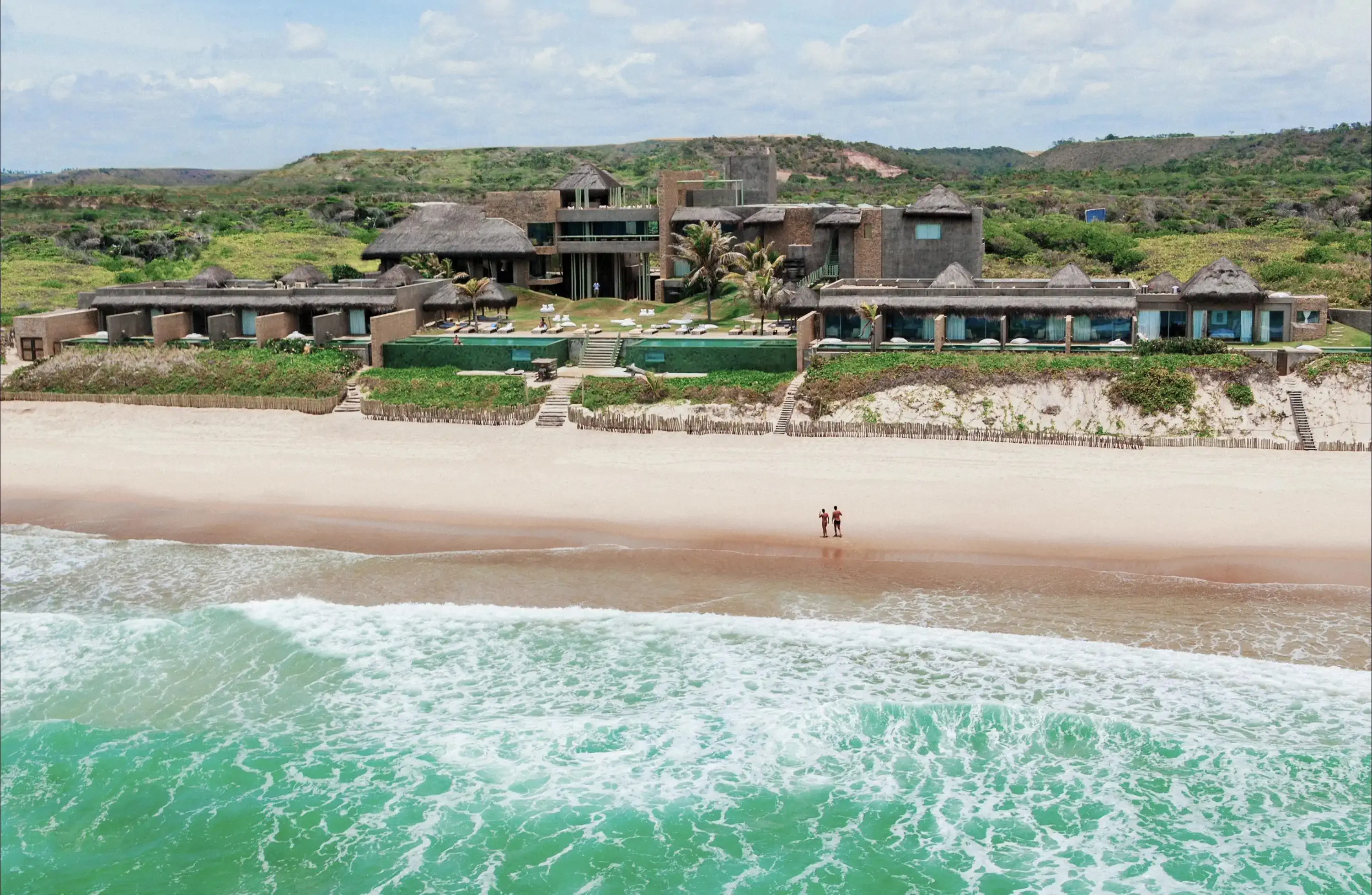 a beach with two people walking in the sand and a hotel in the background