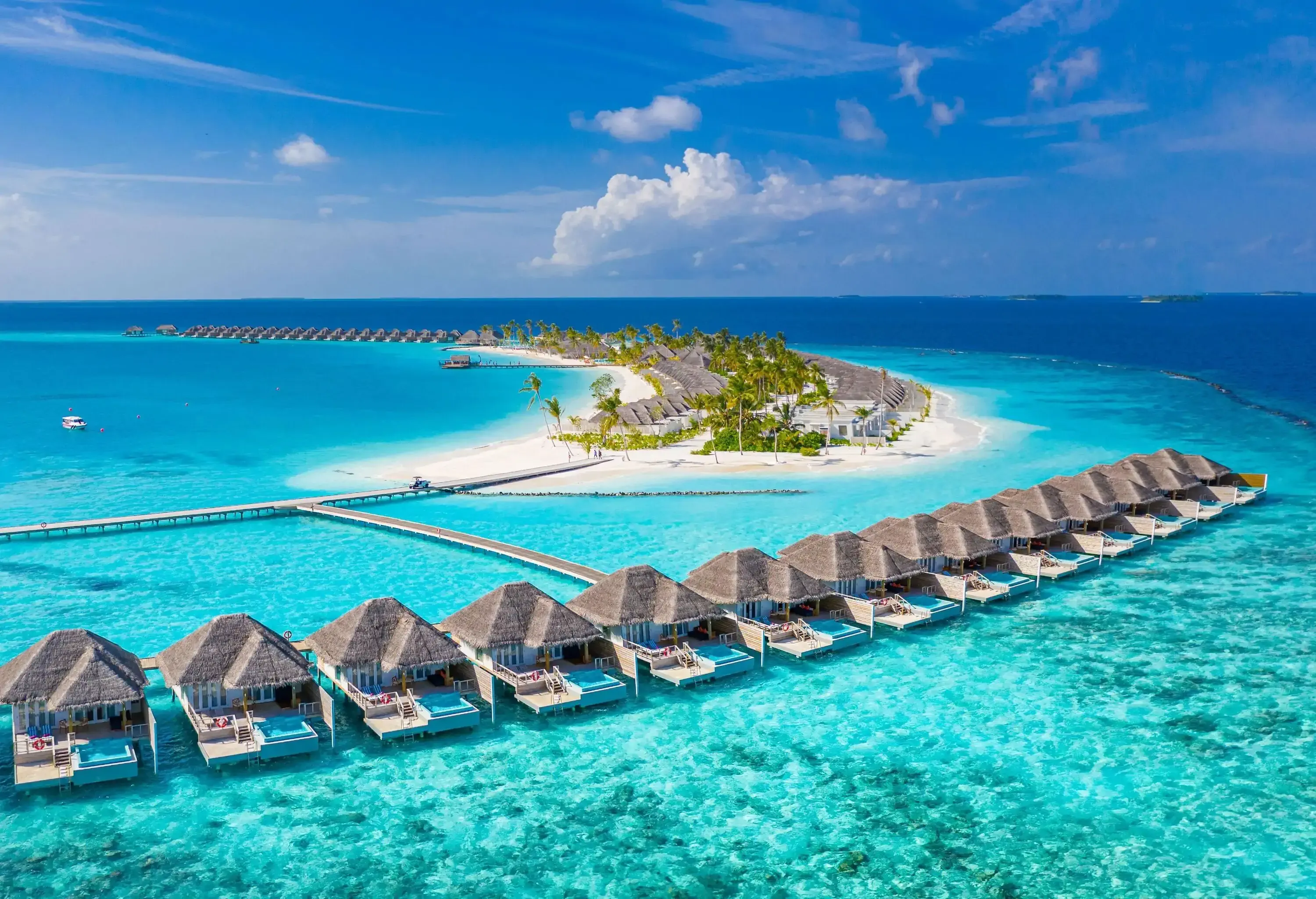 A row of villas with thatch roofs floating across the turquoise waters of the sea.