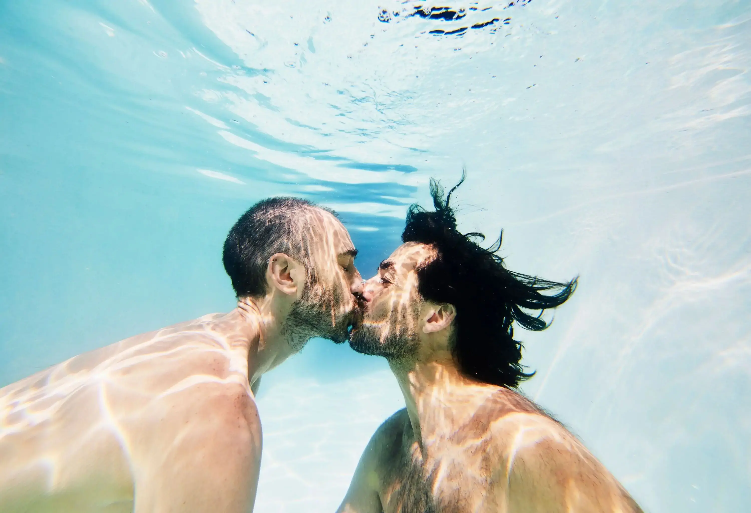 A gay couple kissing underwater in a pool.