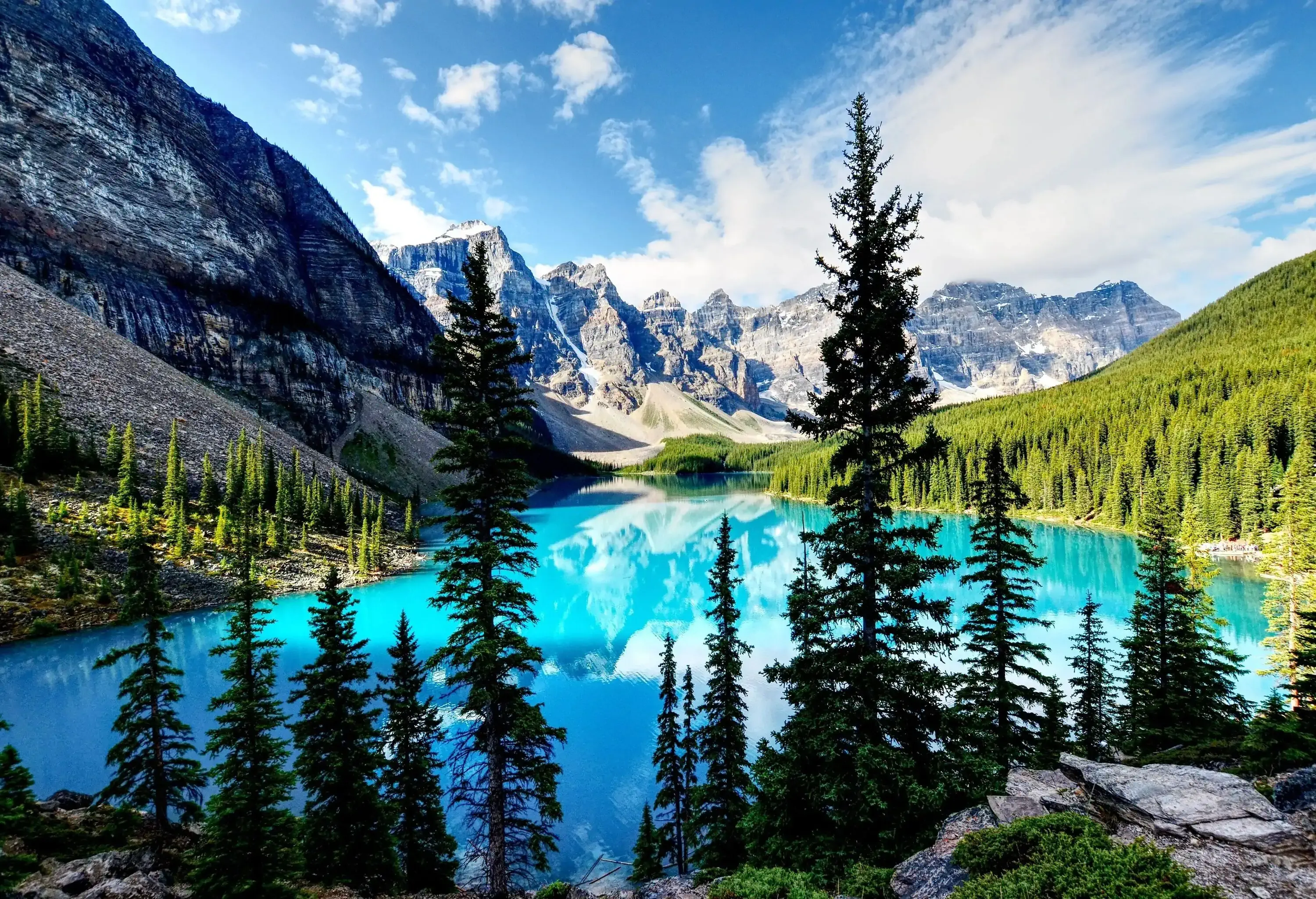 A turquoise water lake lined with tall green trees in the valley of the rocky mountains.