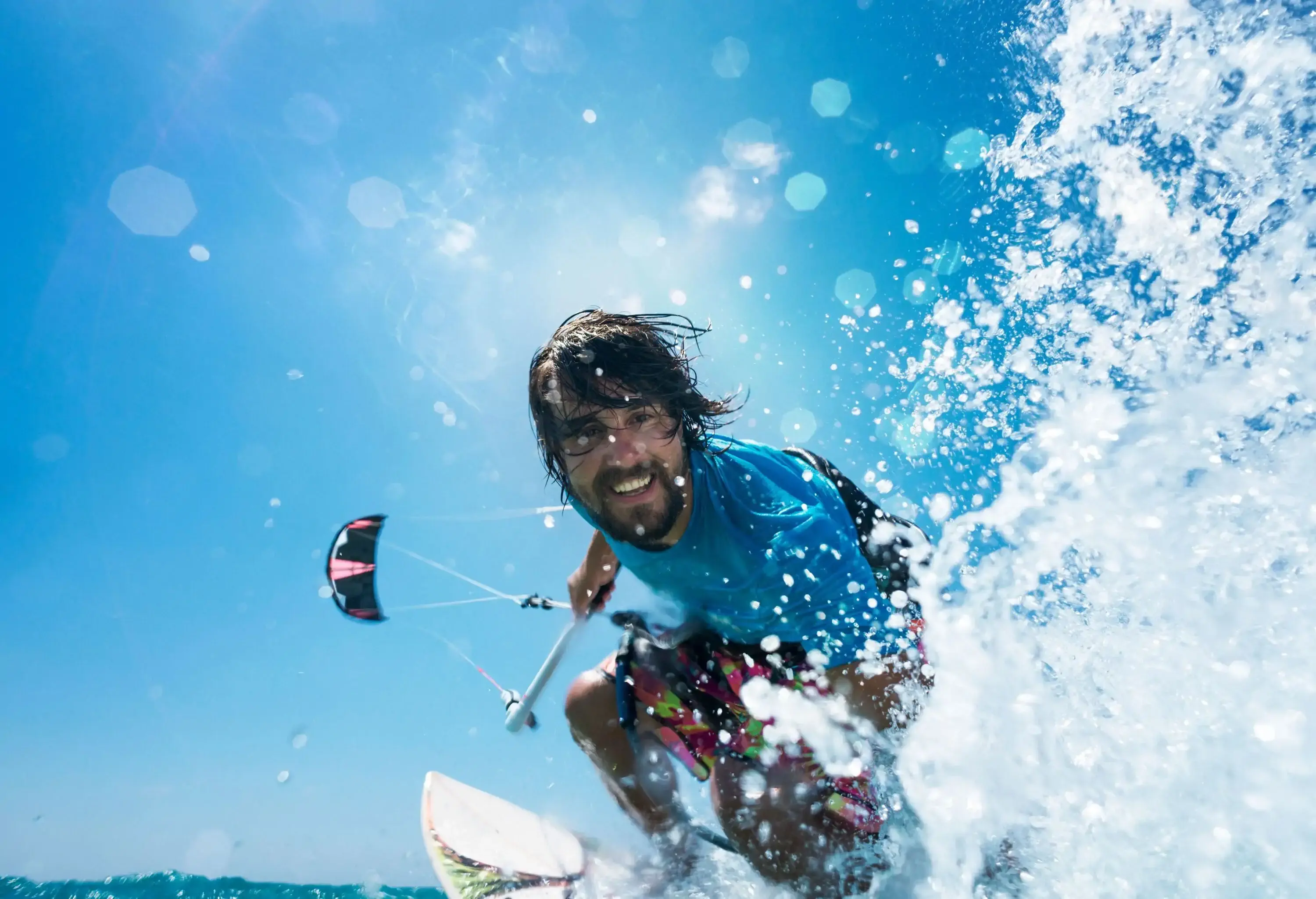 A bearded man smiles as he rides the ocean waves while kitesurfing.