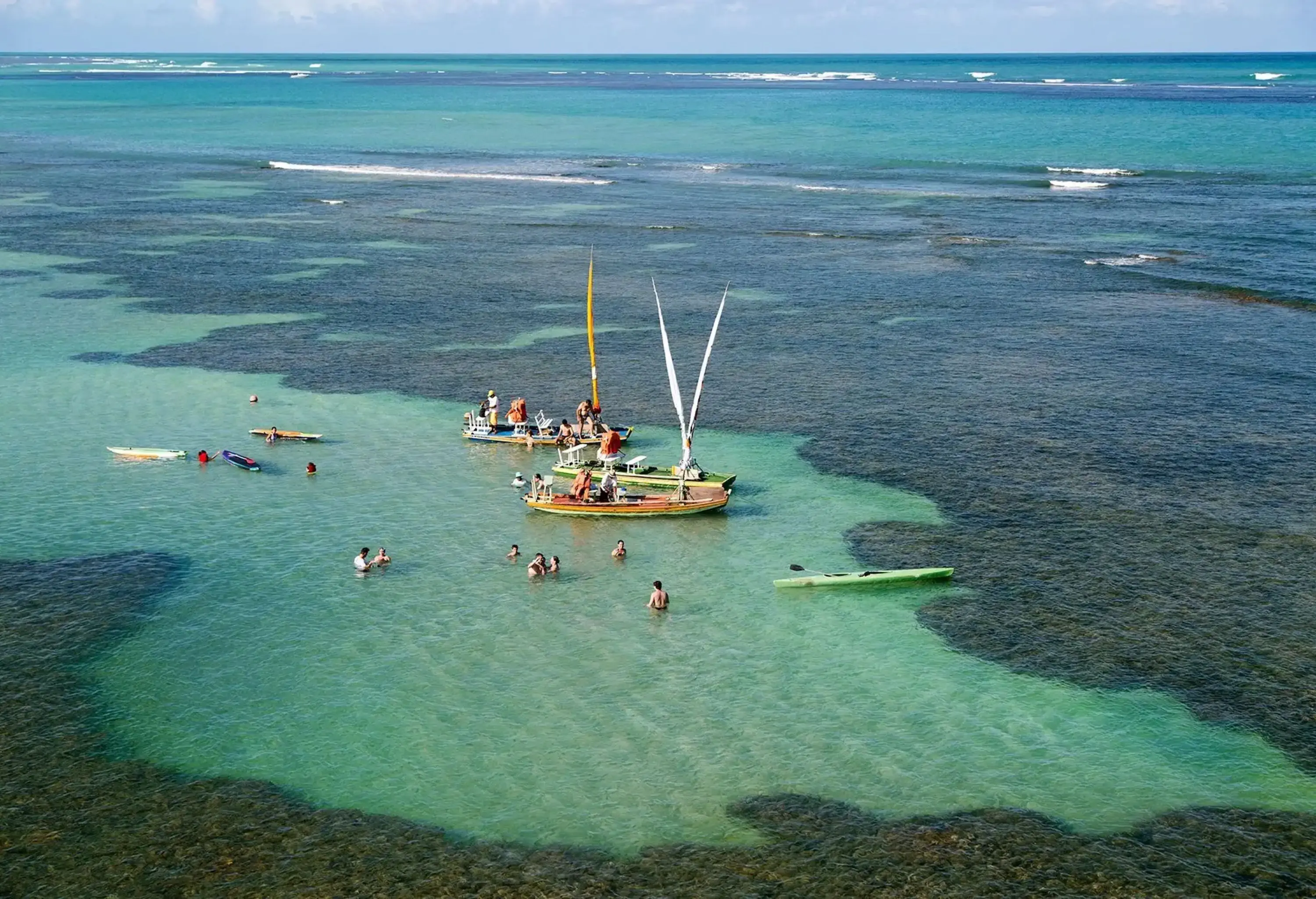 Aerial view of a coral reef in the ocean with a boat standing in the middle and swimmers