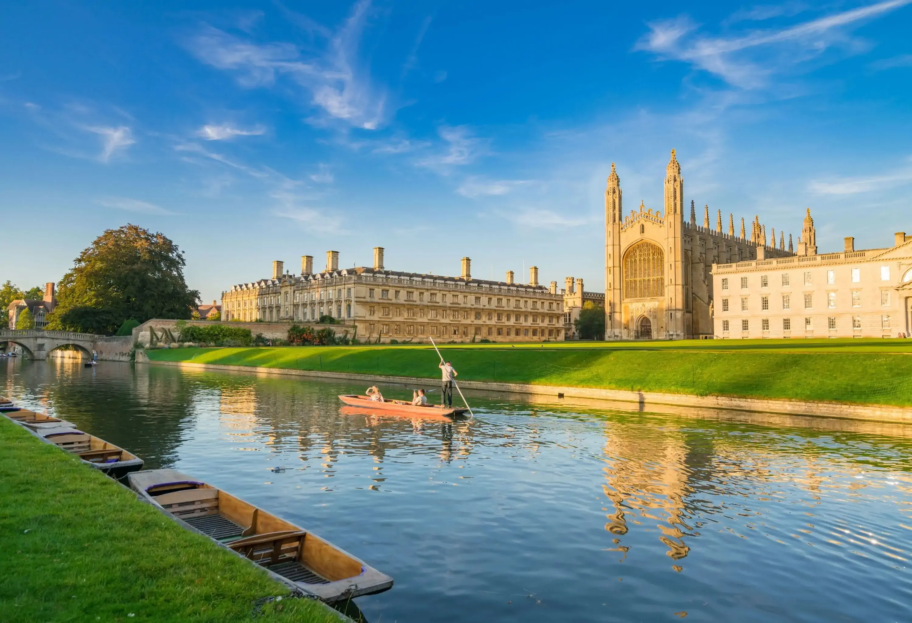 A punting cruise on a river along grassy banks with the University of Cambridge in the backdrop.