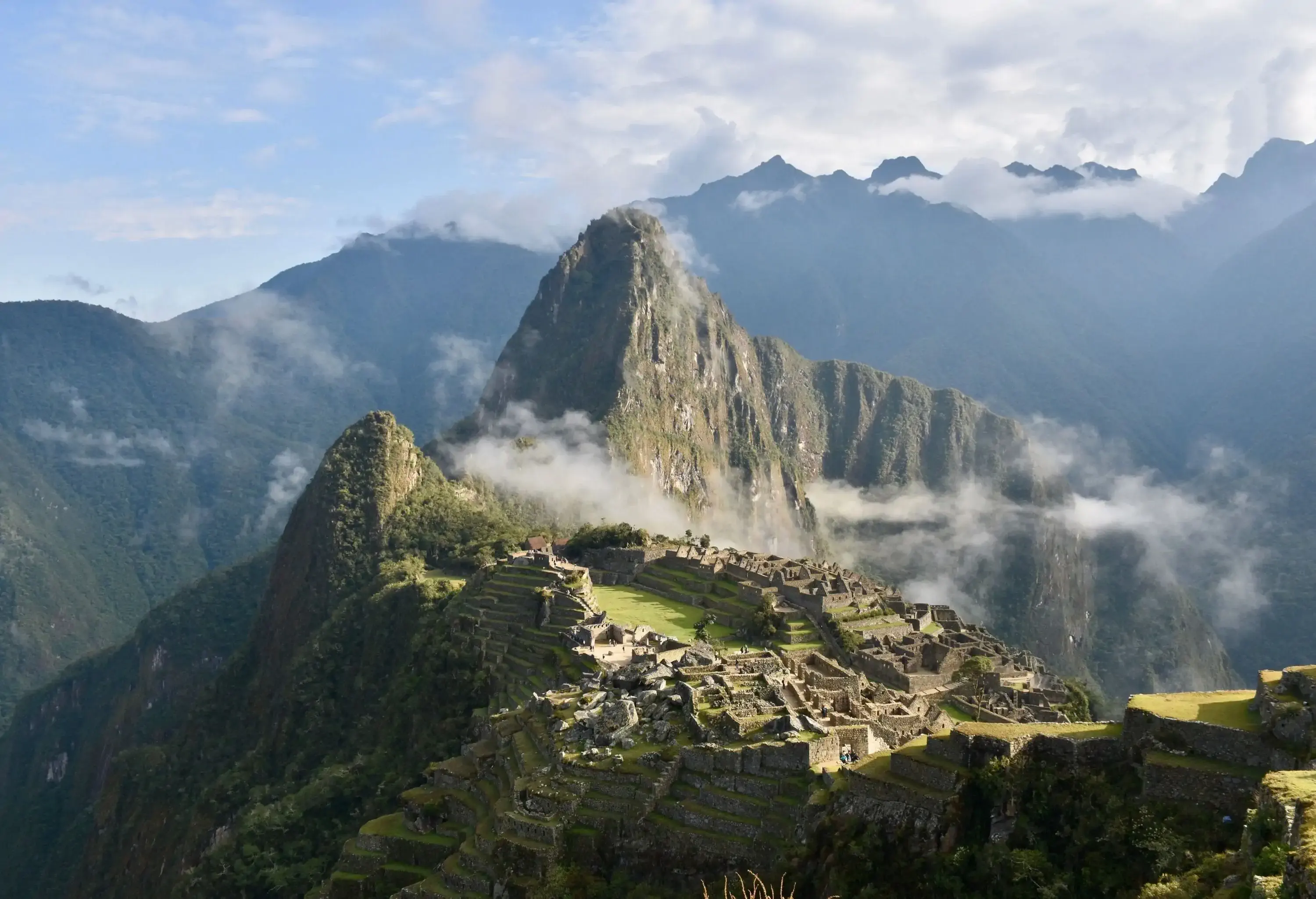 Machu Picchu is an ancient city with ruins perched on a hilltop surrounded by foggy mountains.