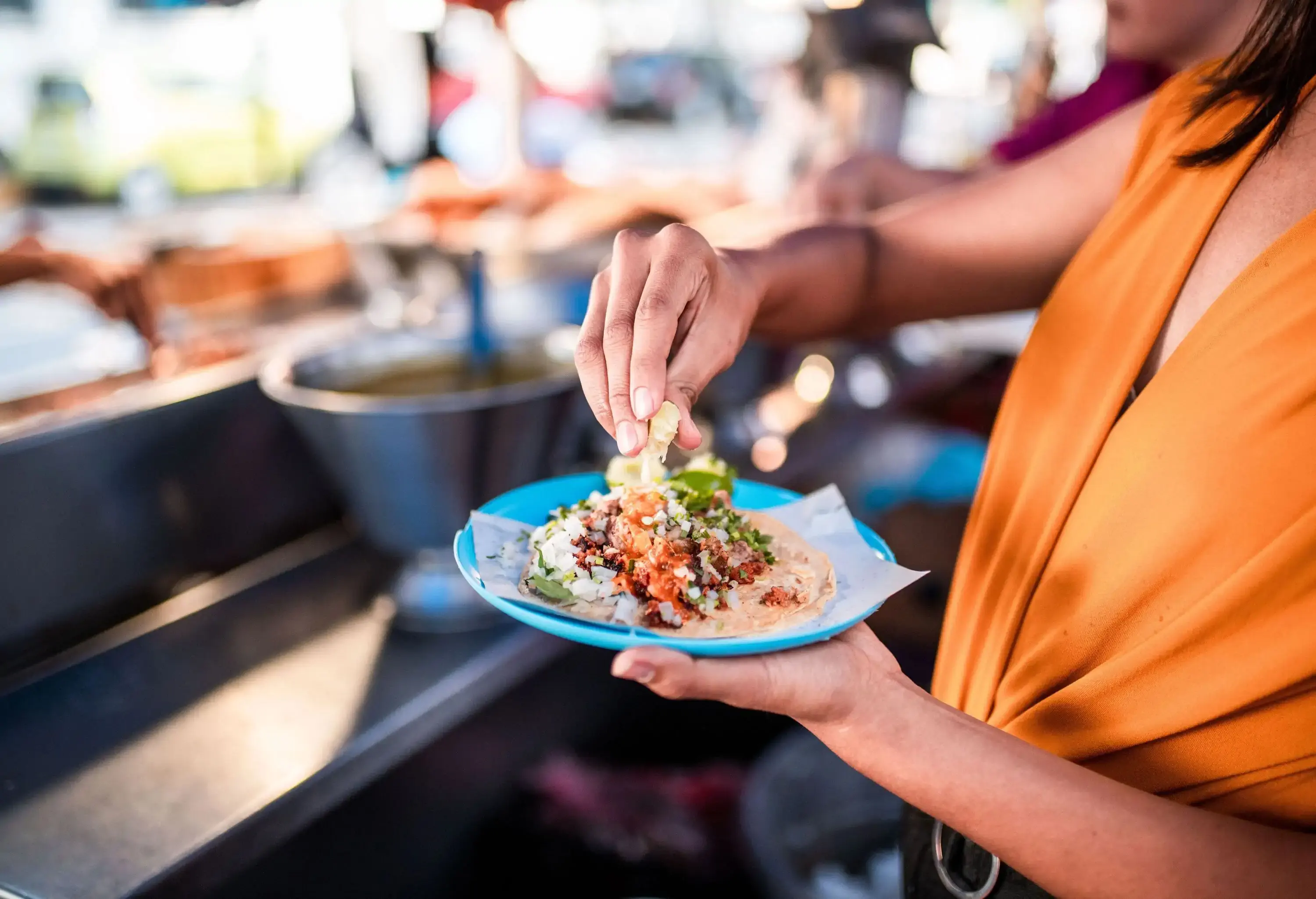 A woman squeezes lime on a plate of meat-filled taco.