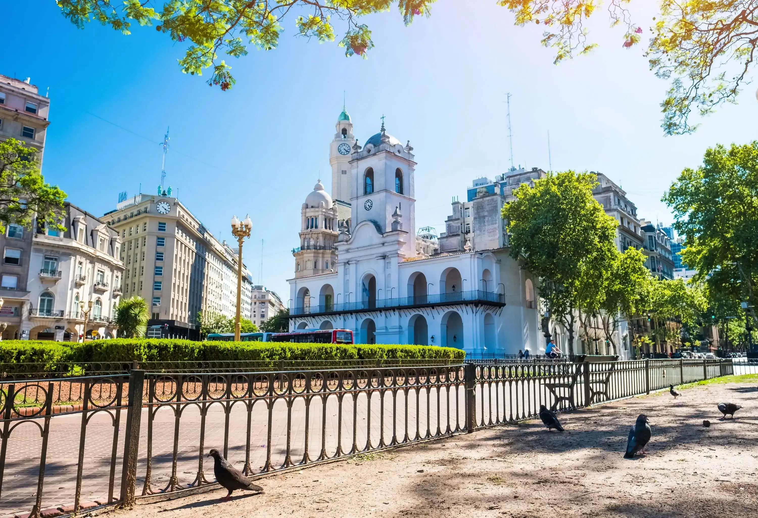 Pigeons are on the grounds adjacent to a white Baroque museum building crowned with a tower clustered with other tall structures. 