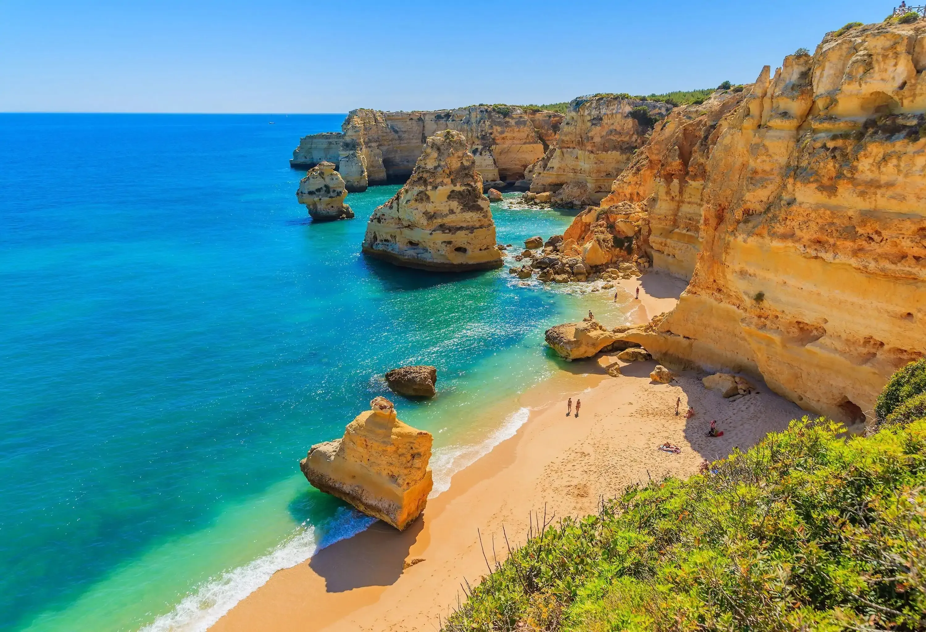 A cove surrounded by cliffs and rock formations with people along the shore.