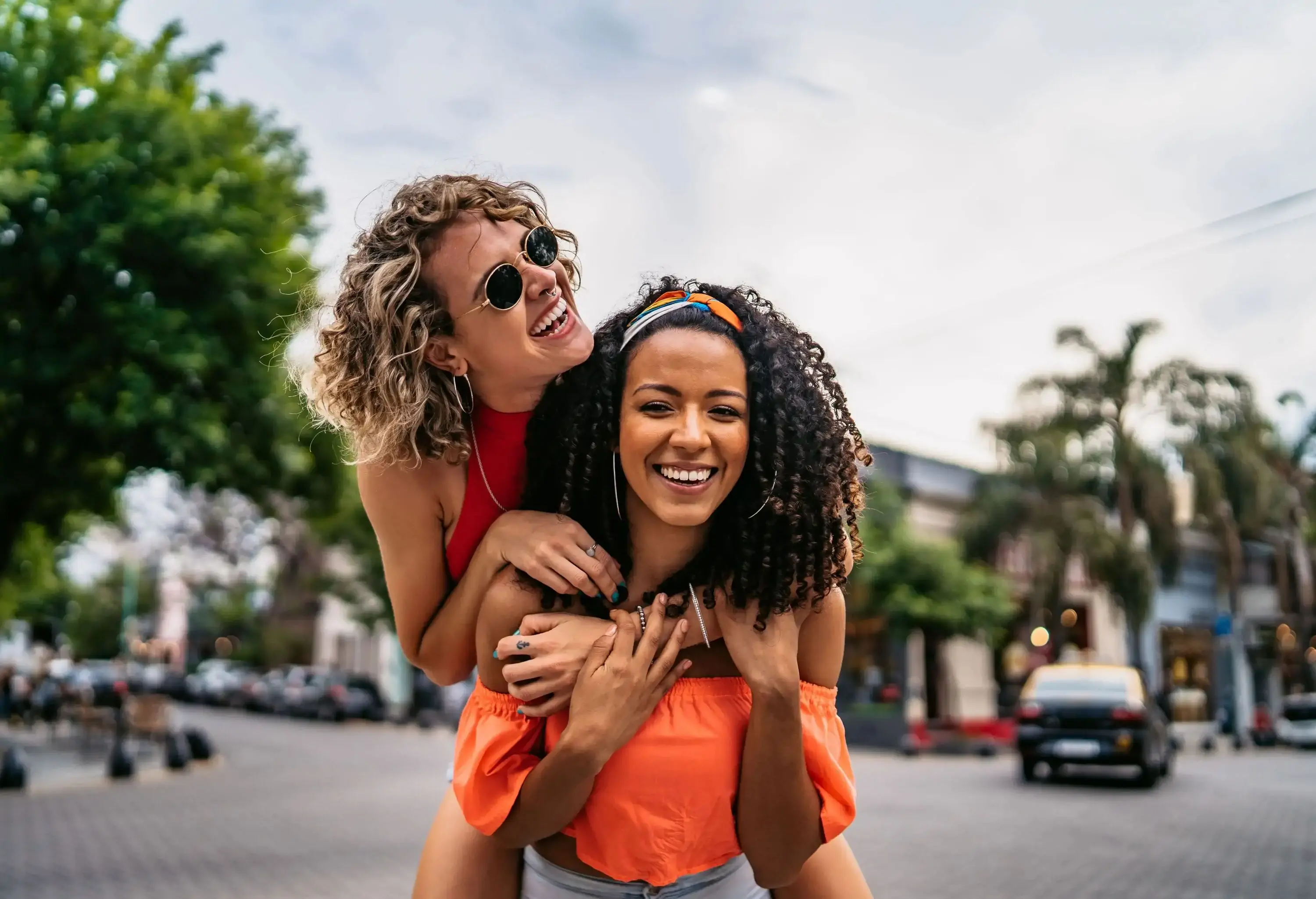 Two young beautiful smiling Argentinian women having fun at city street, having a piggyback ride. Shooting Buenos Aires, Argentina.