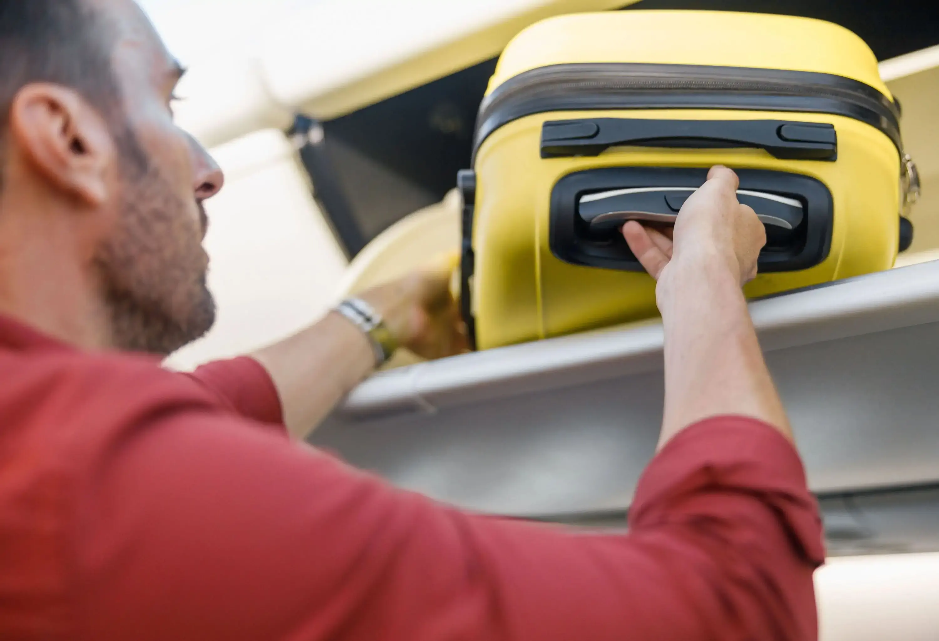 A man taking out a yellow suitcase from an aircraft's overhead bin.