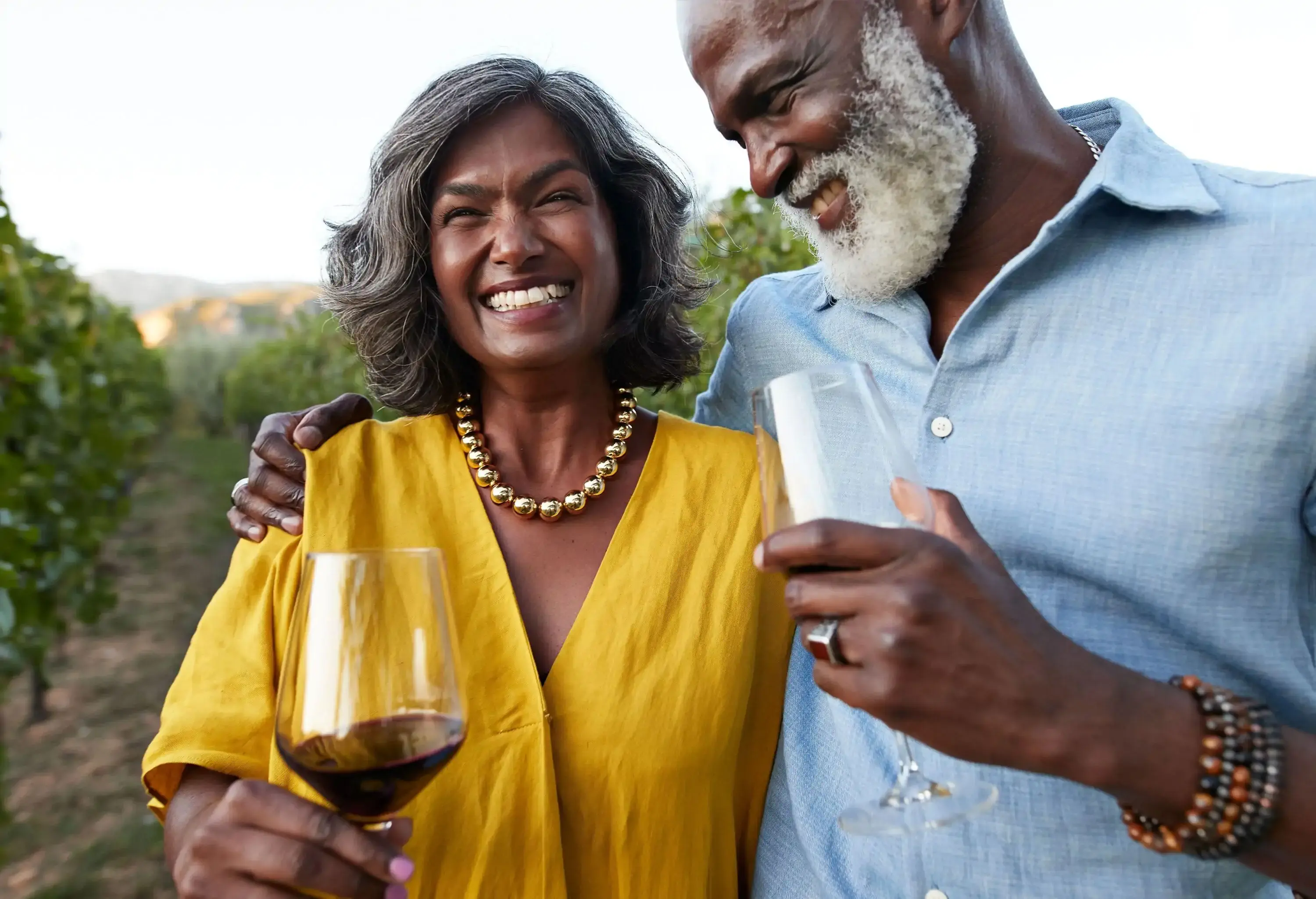 Happy couple with wineglasses enjoying sunset in vineyard on weekend