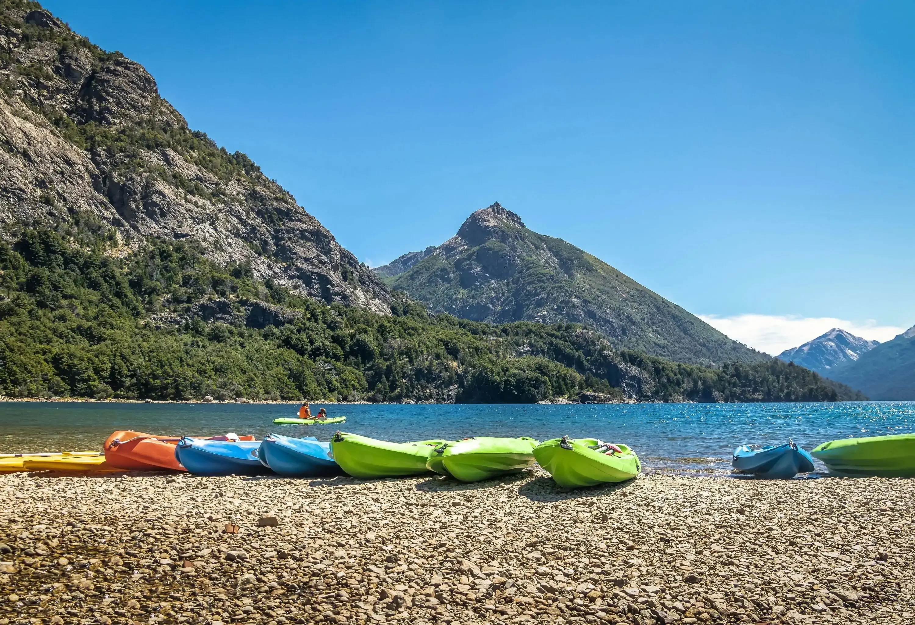 Colourful canoes parked on the pebbly shore of a lake surrounded by steep mountains.