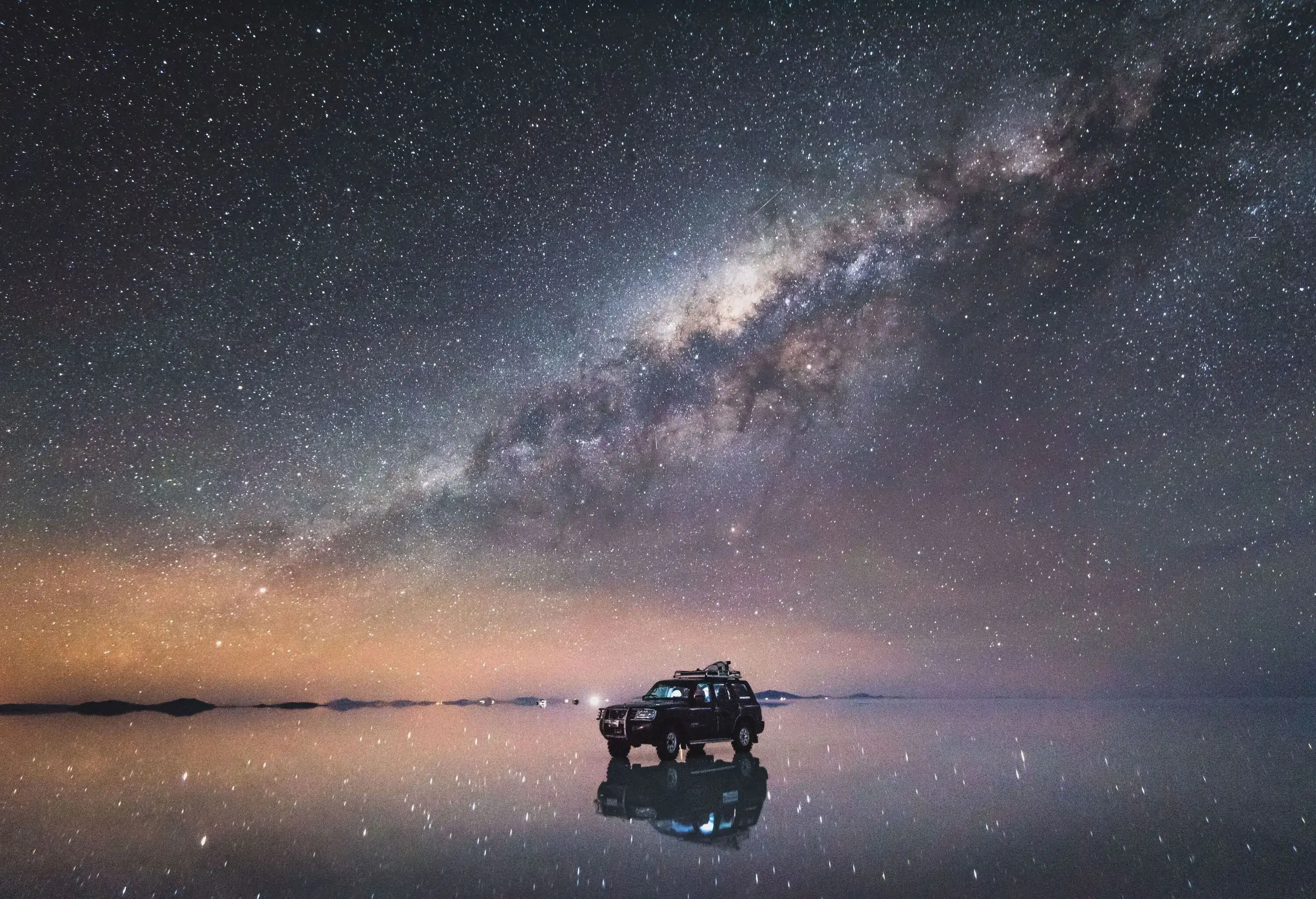 A black parked car on a lake under a constellation of stars.