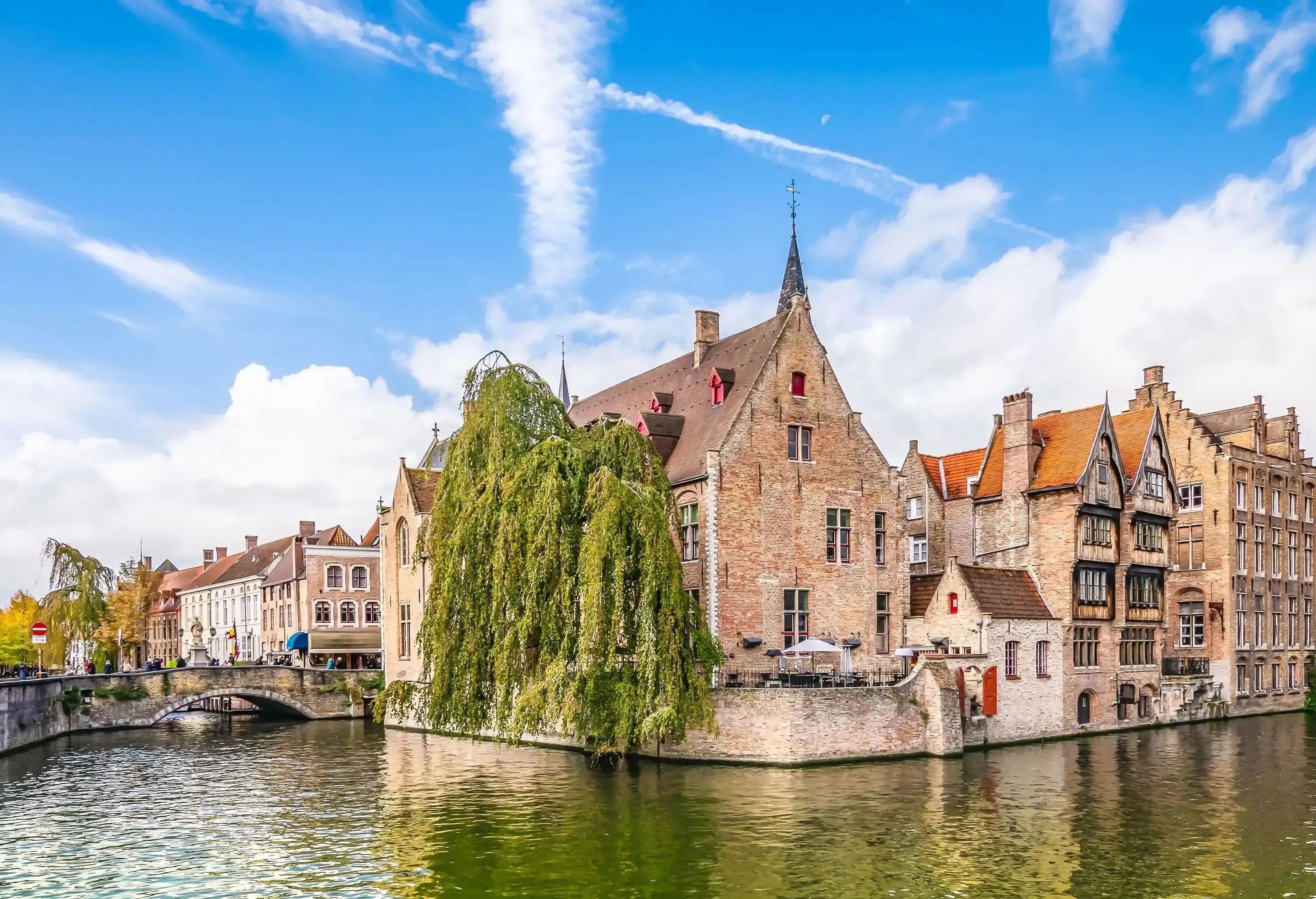 A brick tower topped with a spire and a medieval octagonal upper stage bell tower easily seen protruding above the roofs of surrounding buildings on the river bank.