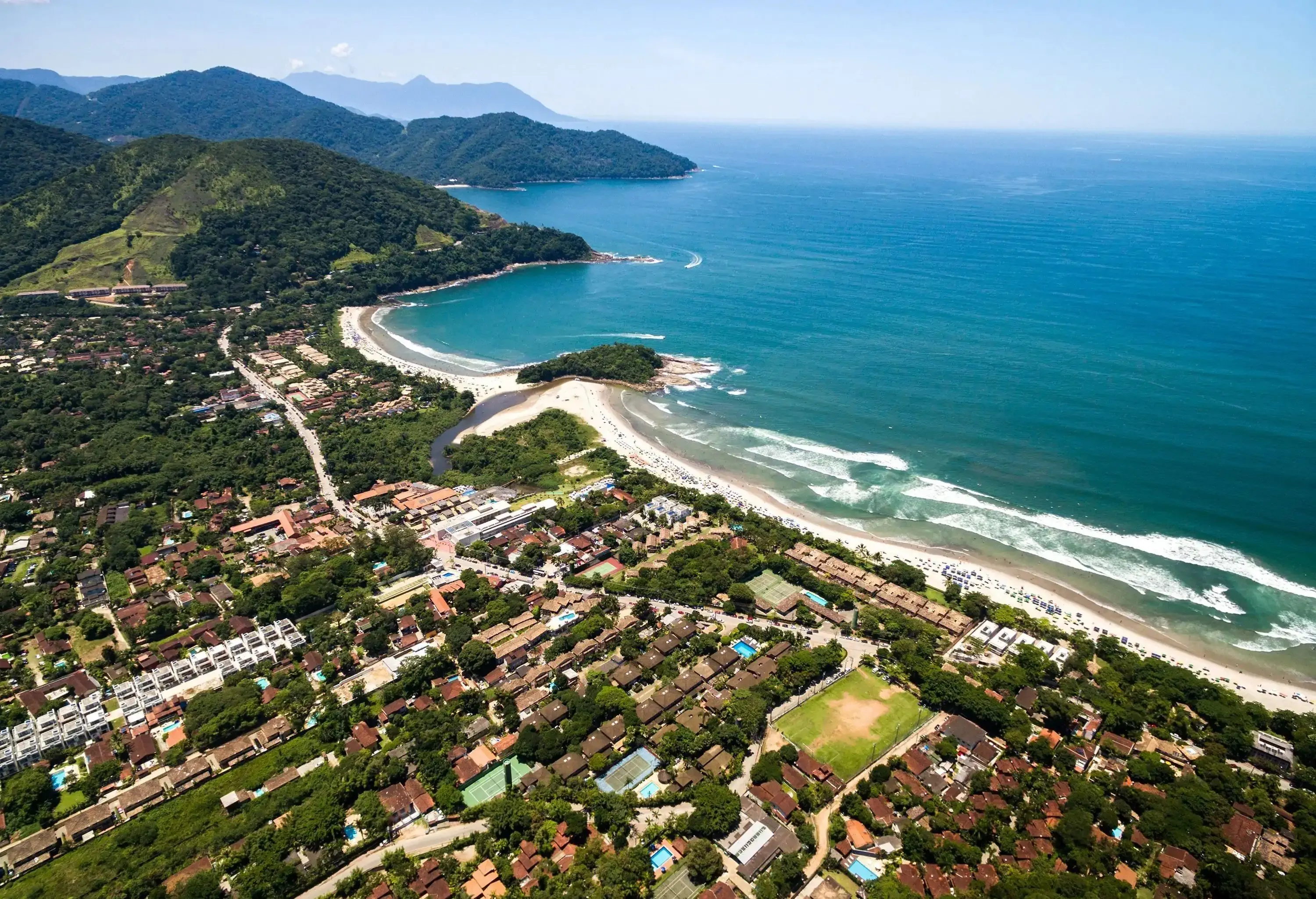 A quaint coastal town boasts tree-lined streets, while the serene beauty of wooded hills unfolds in the distance.