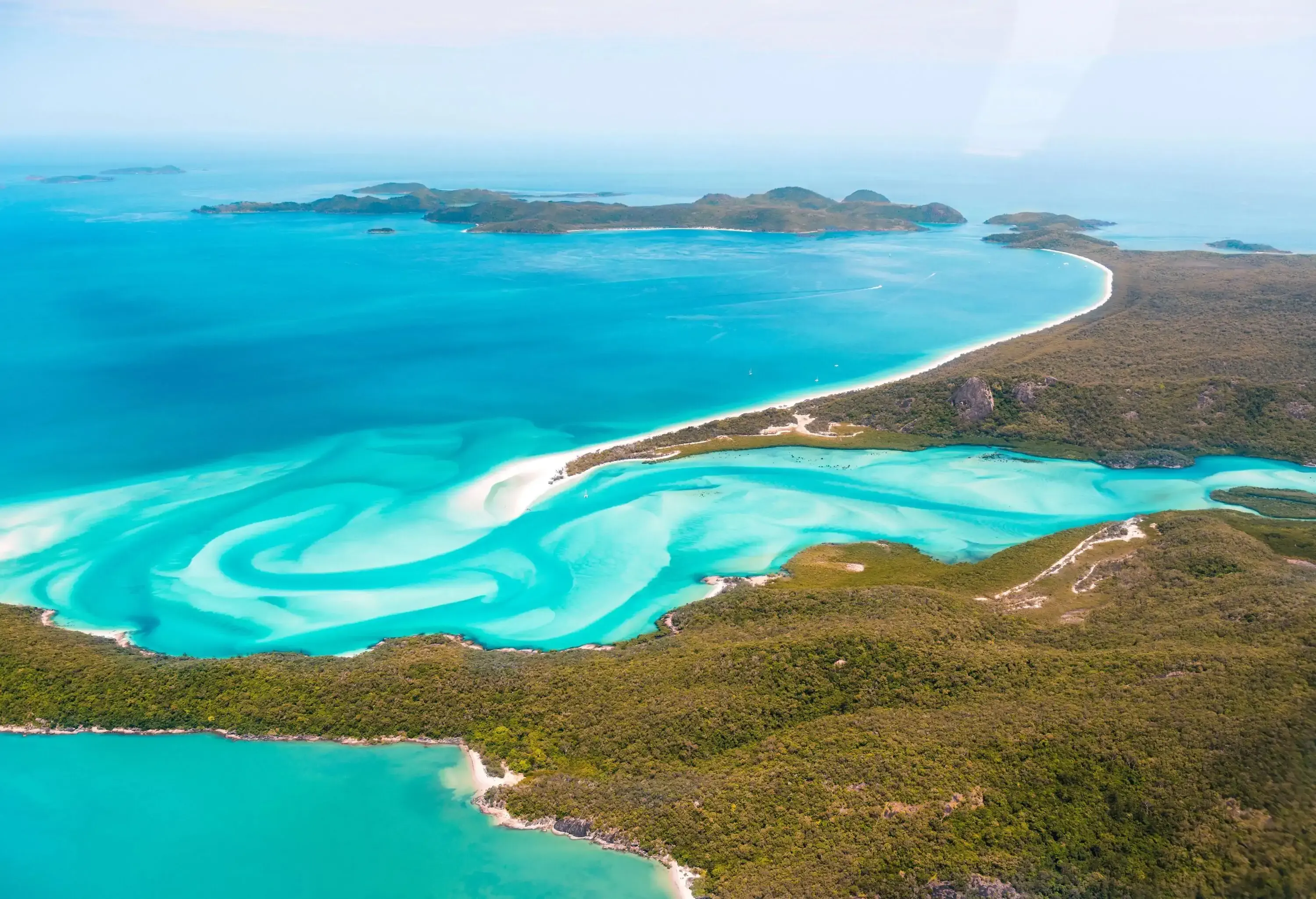 Soft white sand gently blending with perfect blue seawater bordered by woodlands.