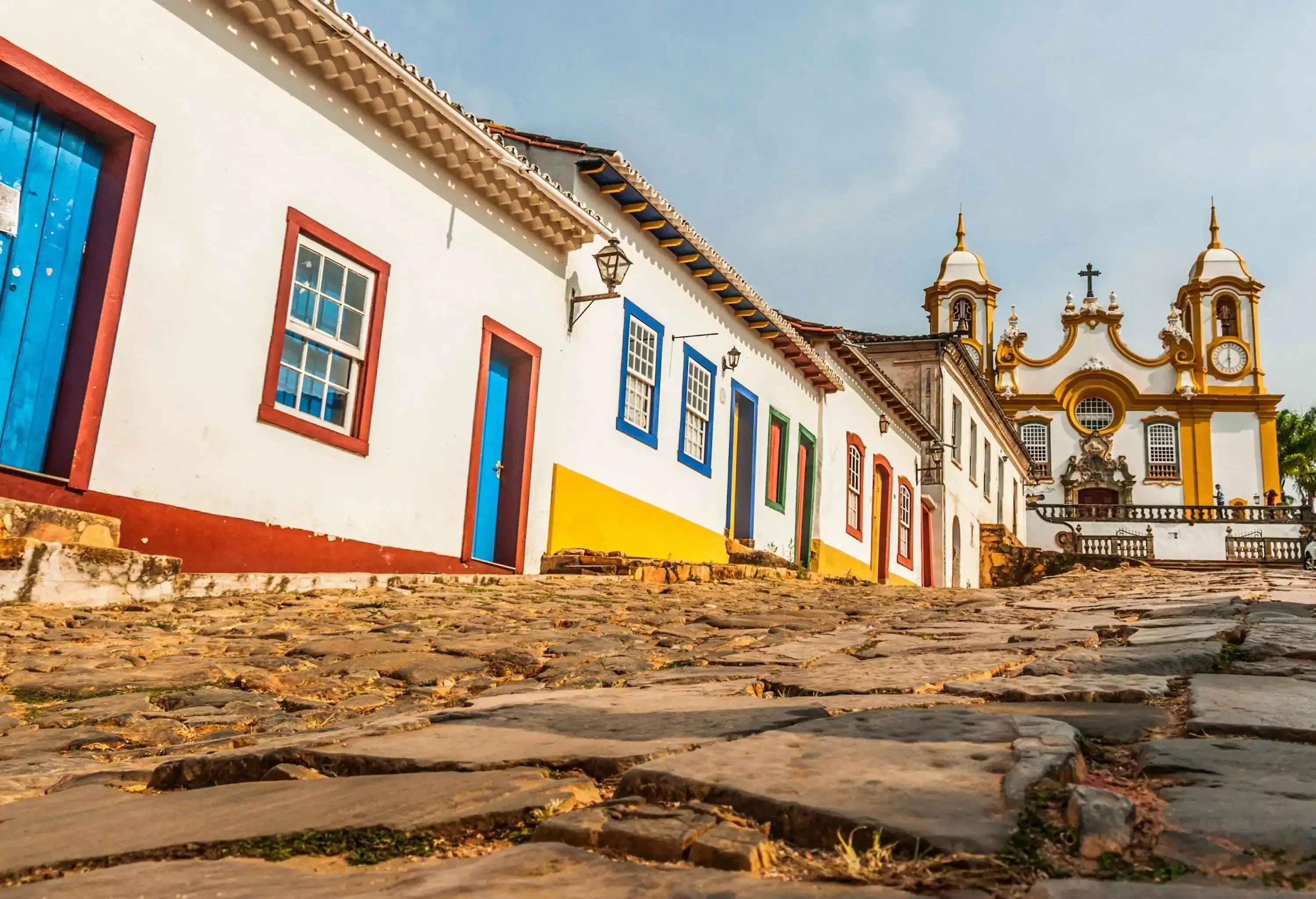 A row of white houses with multi-coloured lining of windows and doors sloping on a rugged path approaching a church atop.