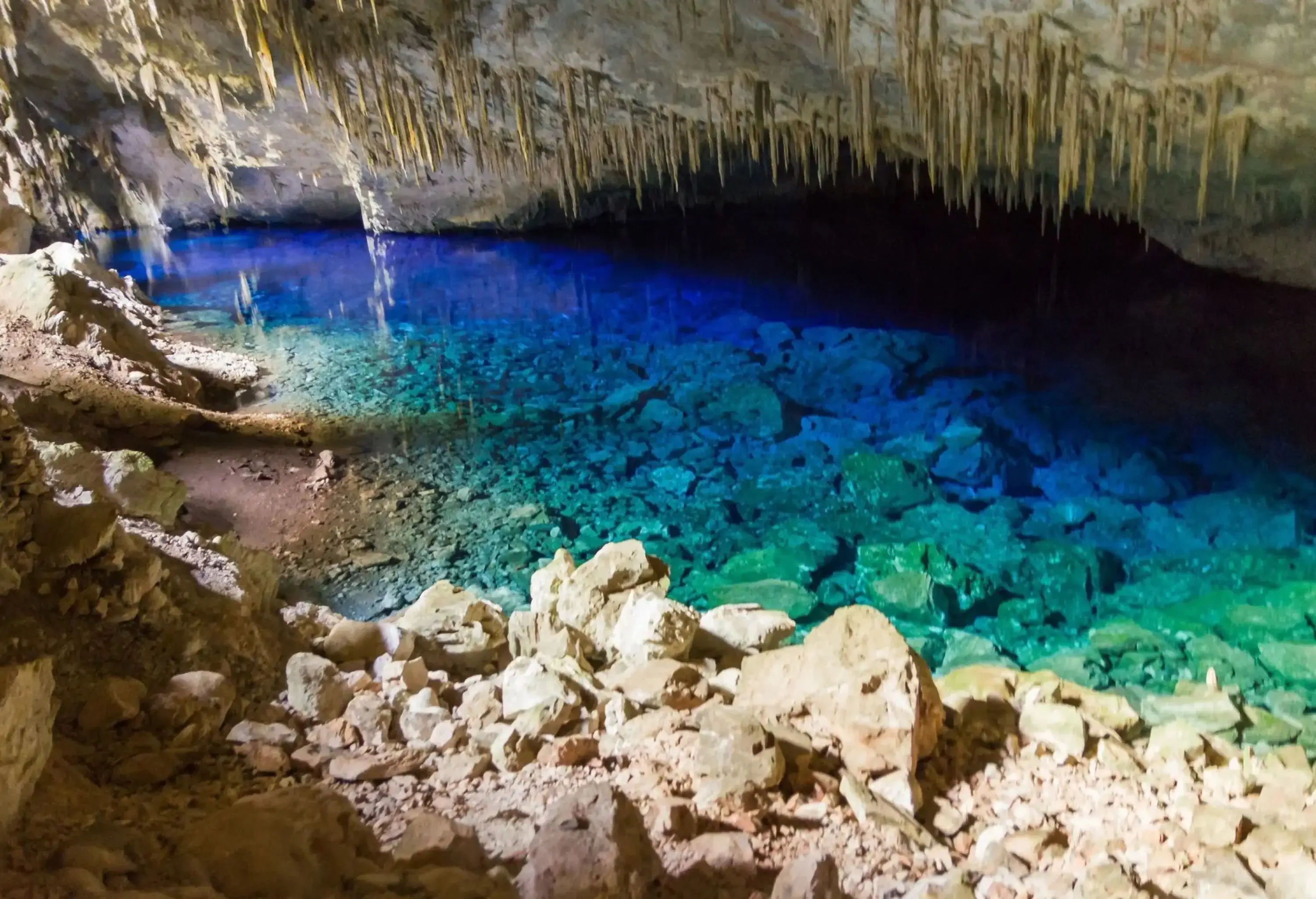 A blue lagoon inside a rocky cave under sharp stalactites.