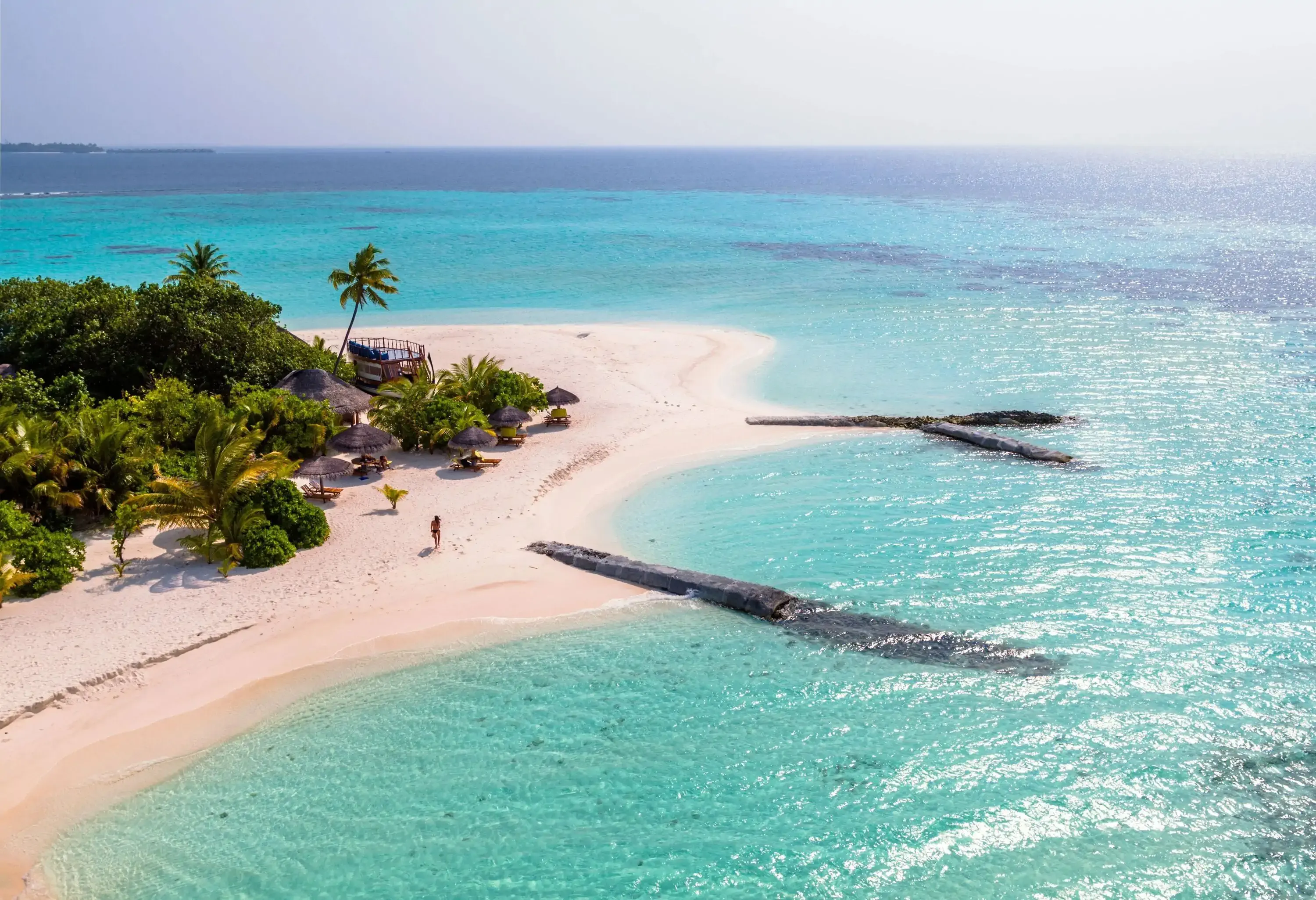 A charming lady in a bikini walking on the small sandy beach surrounded by the crystal clear turquoise sea.