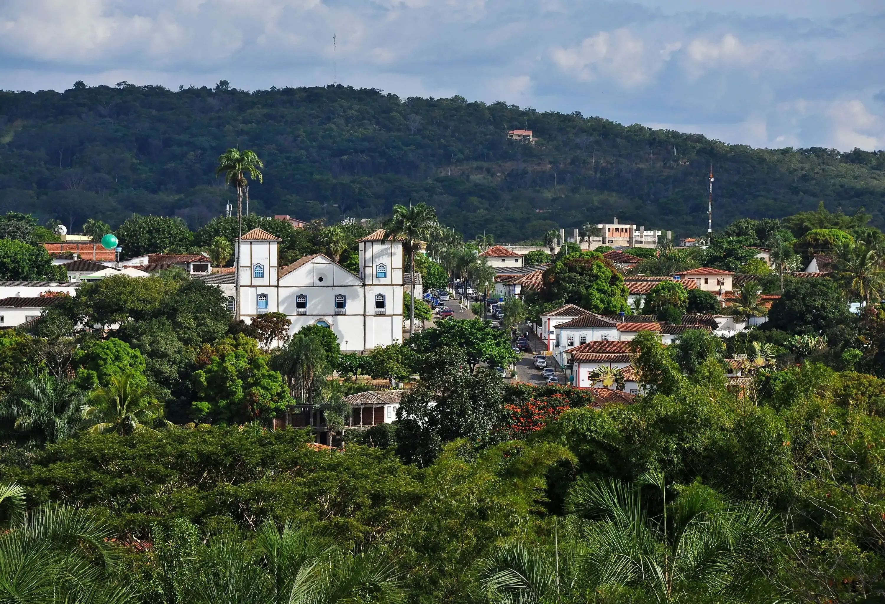 A white church with two towers overlooks a town surrounded by lush vegetation.