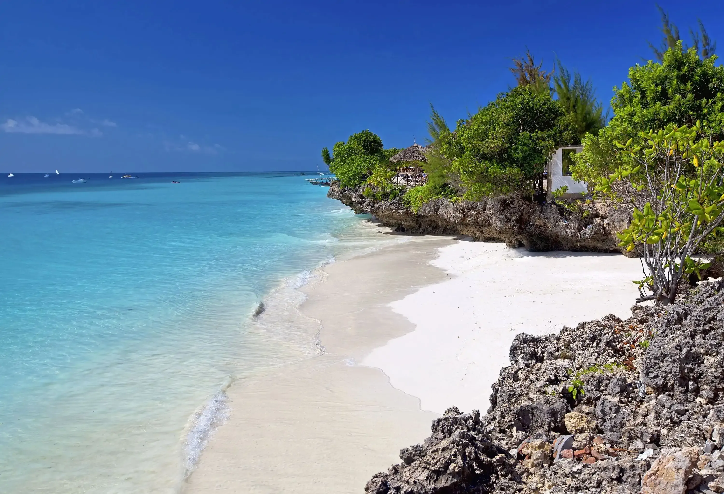 A rocky lush island with a white sand shore surrounded by the clear water sea.