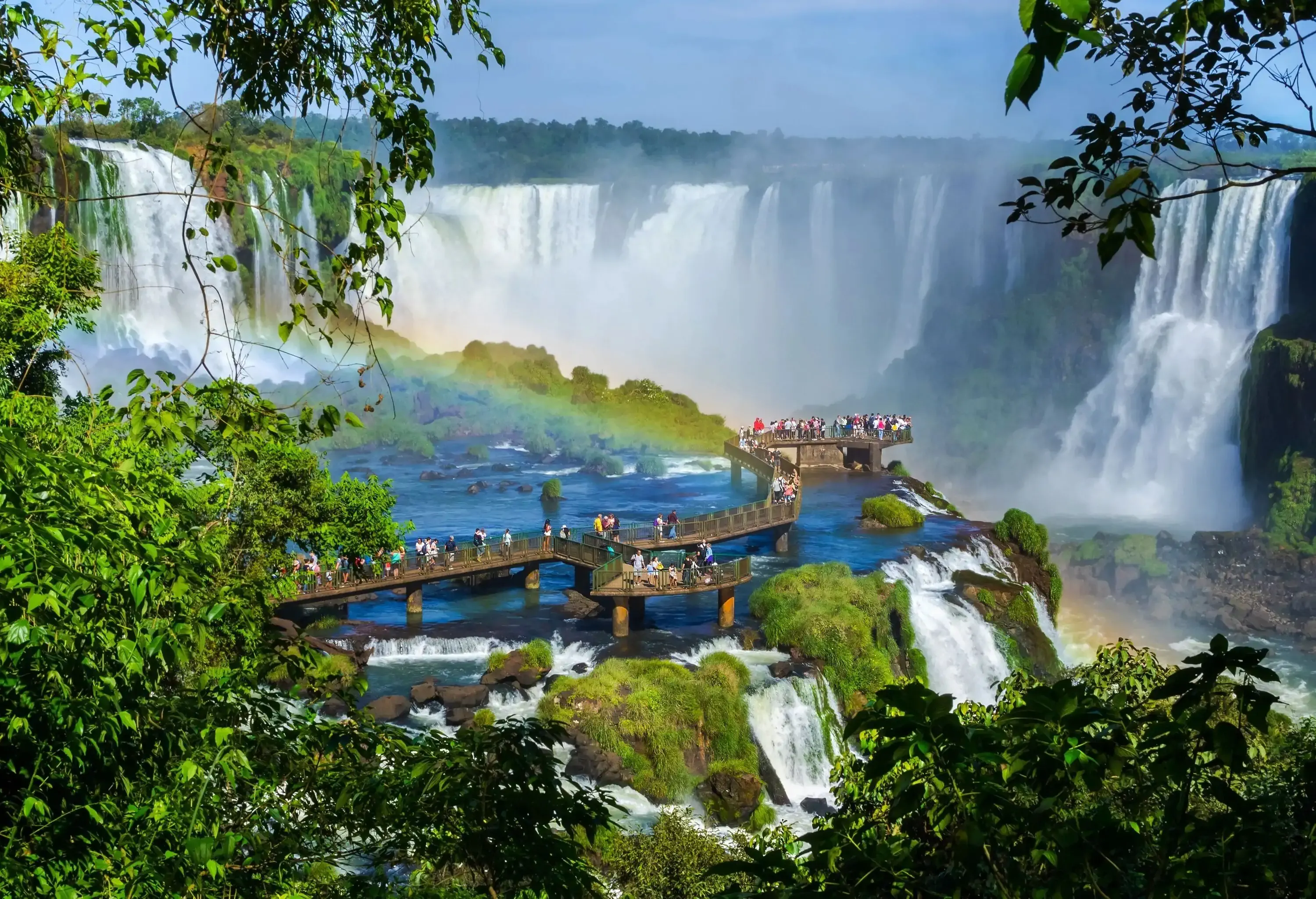 People walking along a footbridge on a cliff surrounded by thunderous cascades.