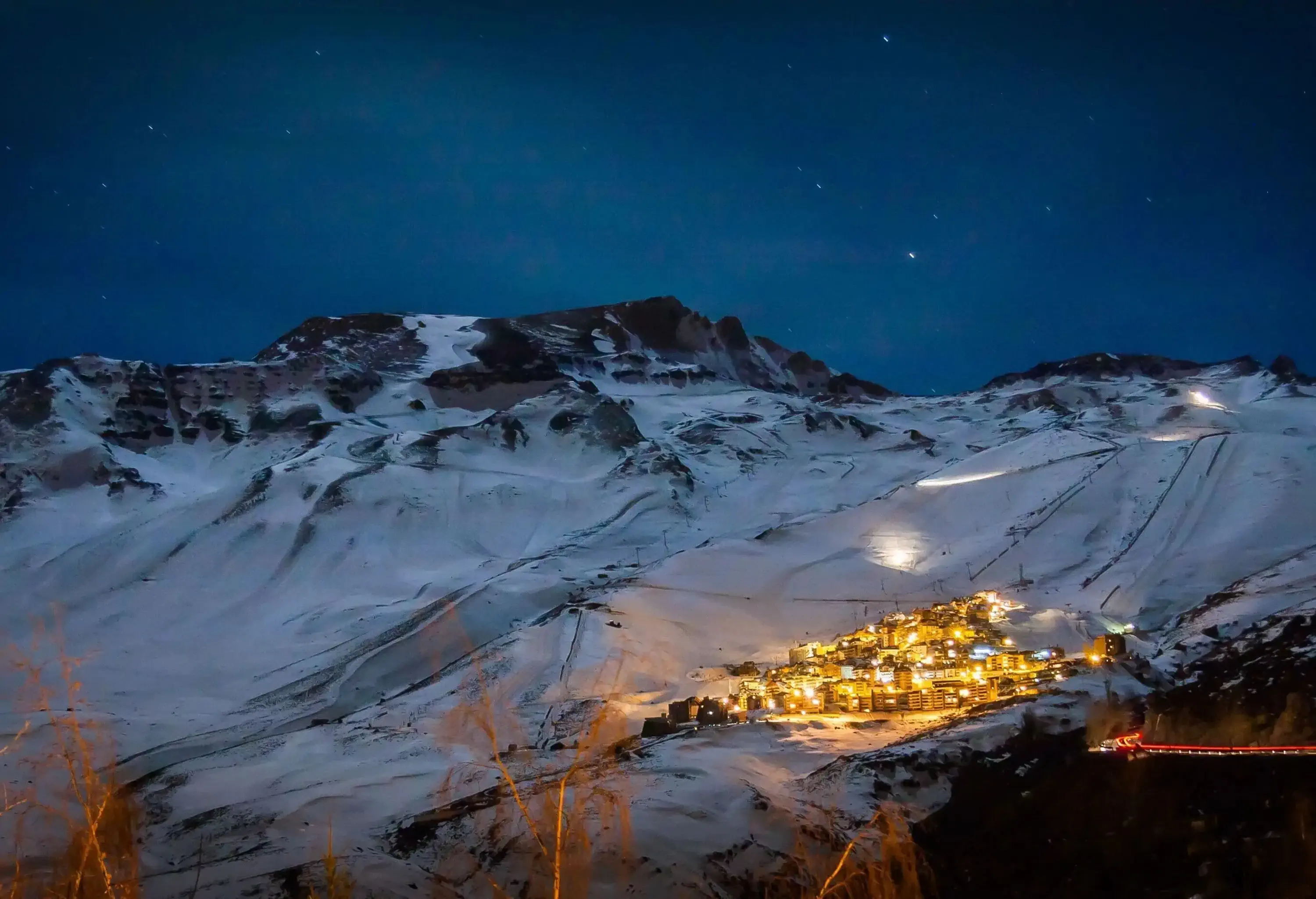 night landscape view of illuminated mountain village surrounded by snowy mountains