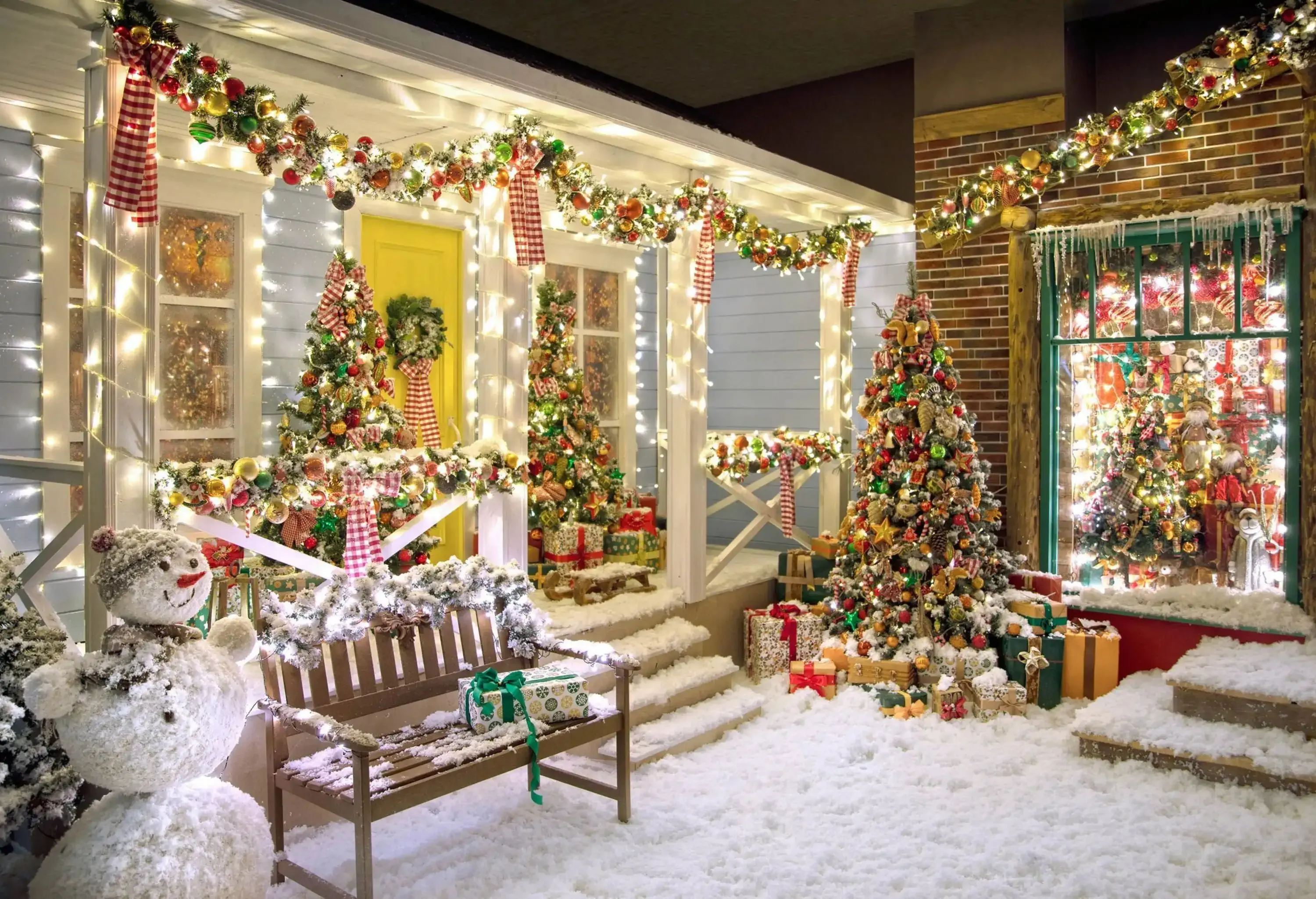 The Christmas theme veranda of a residential home is decorated with a snowman, fake snow, Christmas trees, and boxes of Christmas presents.